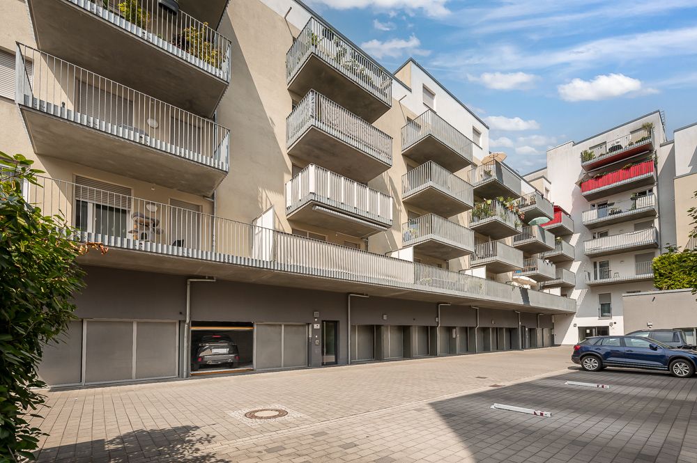Mehrstöckiges Wohnhaus mit Balkonen, Parkplätzen und Garagen im Vordergrund.