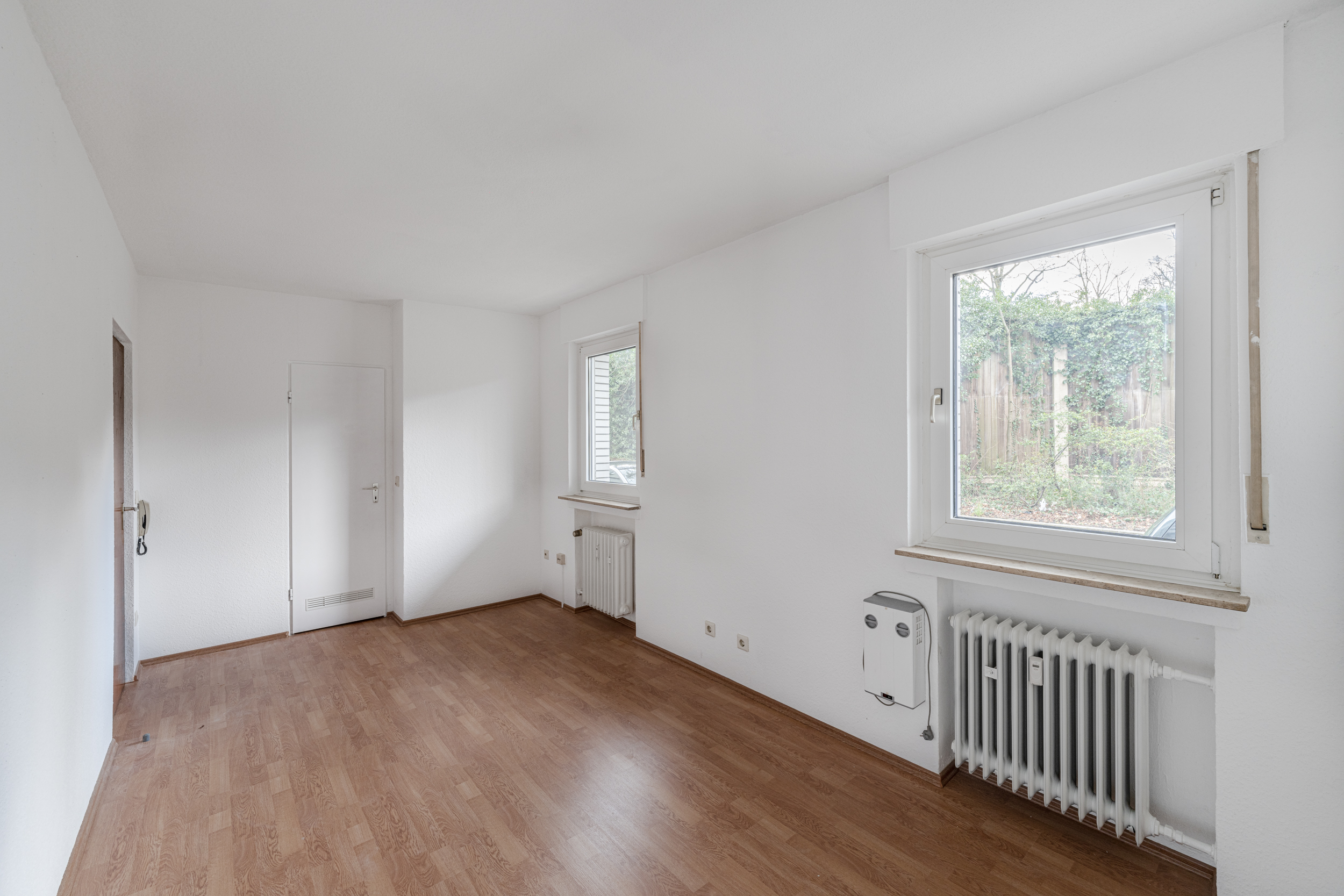 Heller, leerer Raum mit zwei Fenstern, weiß gestrichenen Wänden und Laminatboden.