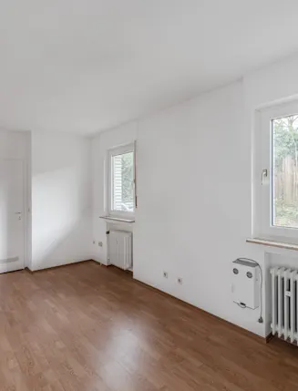 Heller, leerer Raum mit zwei Fenstern, weiß gestrichenen Wänden und Laminatboden.