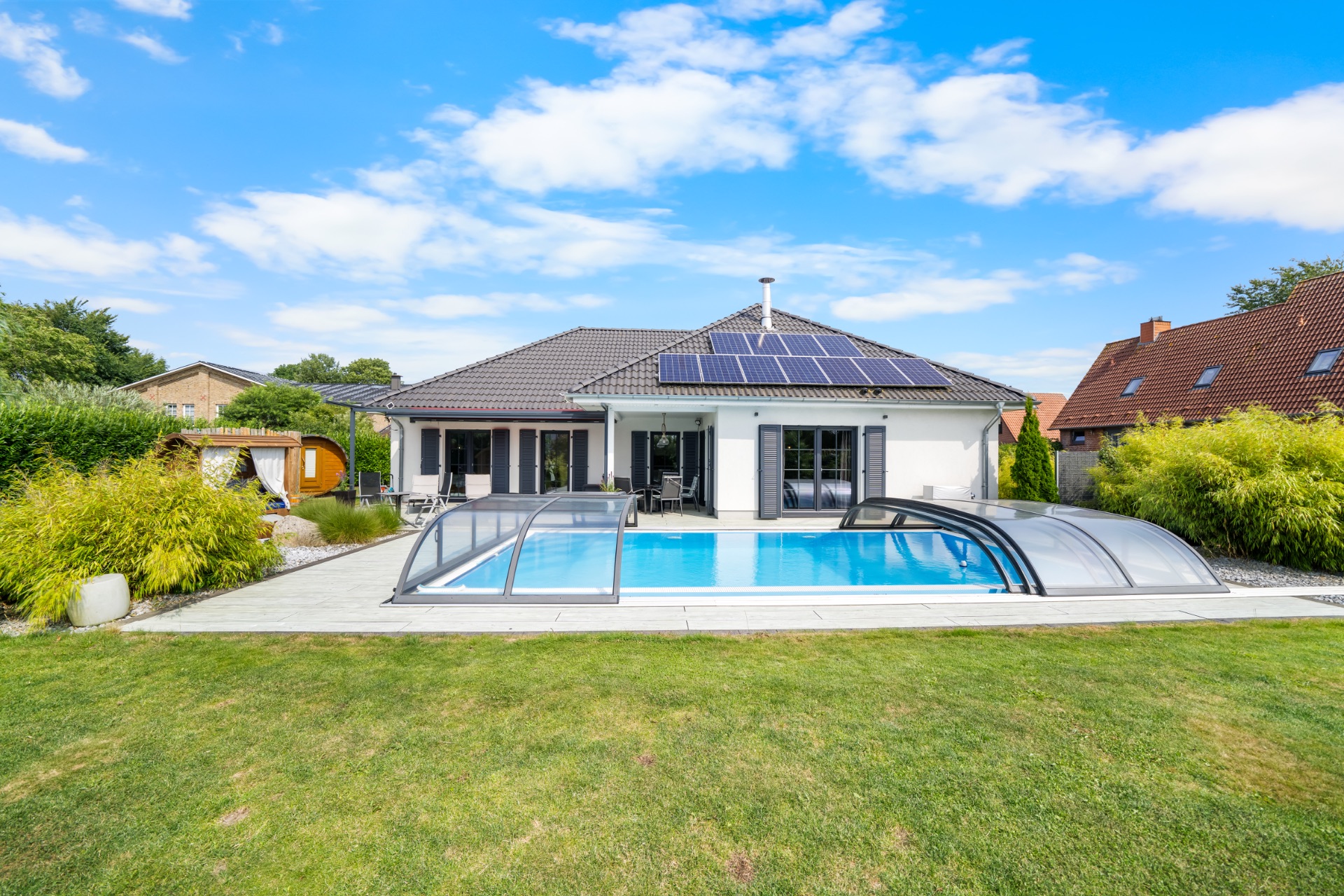 Einfamilienhaus mit Solarzellen und überdachtem Pool im Garten.