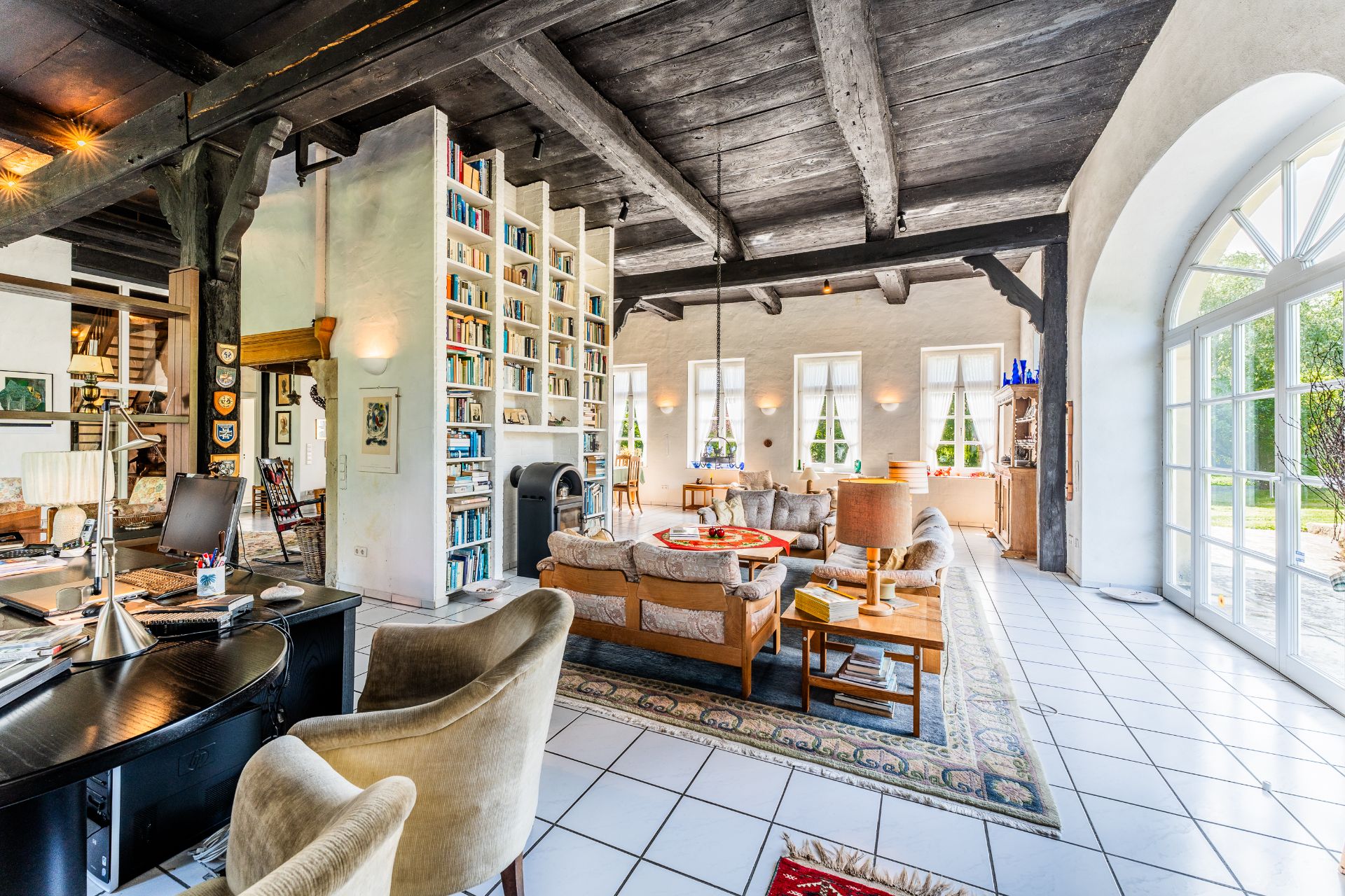 Helles Wohnzimmer mit Bücherwand, Sofas, Schreibtisch und großen Fenstern mit Blick nach draußen.