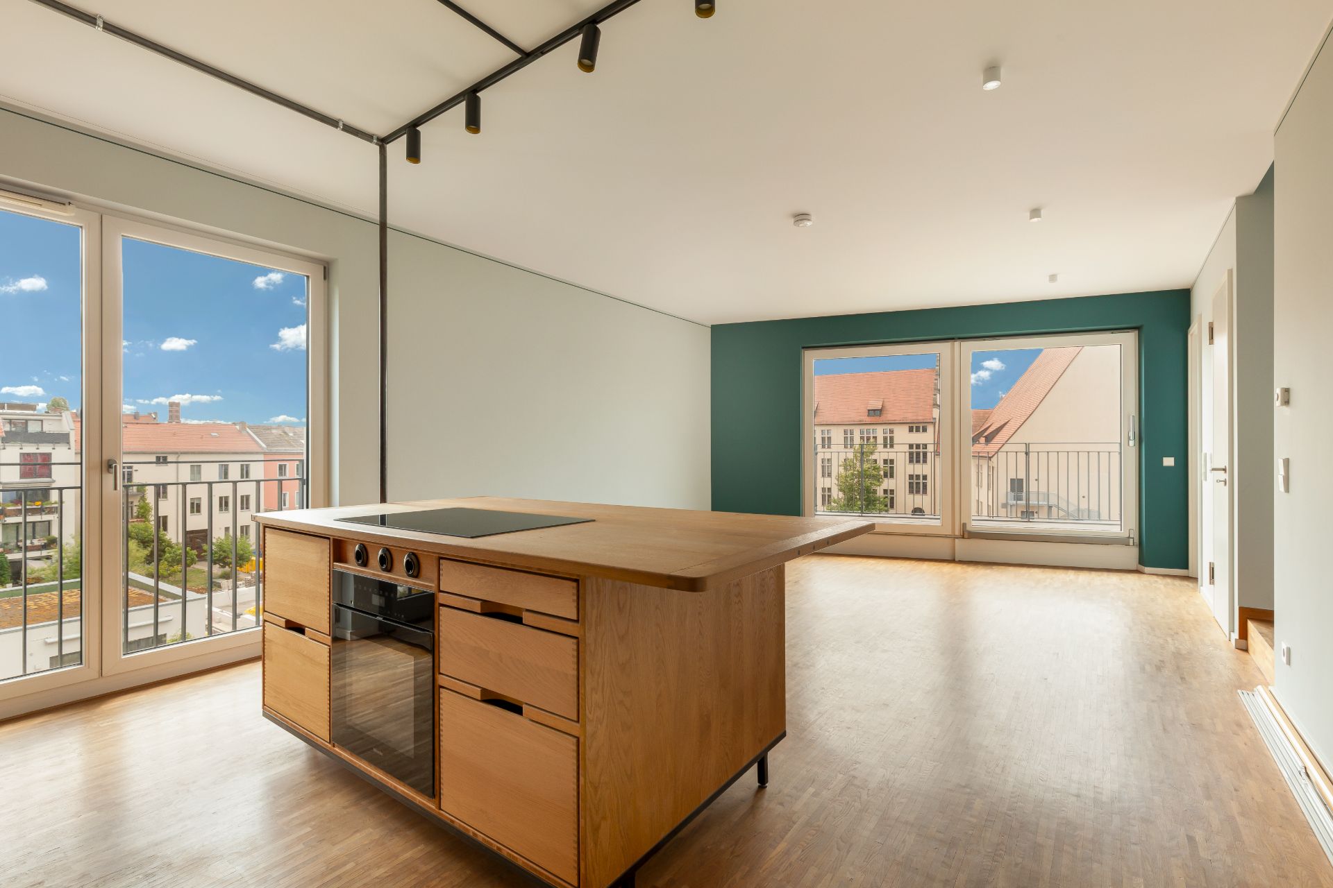 Heller Wohnraum mit Kücheninsel, großen Fenstern und Blick auf Nachbargebäude.