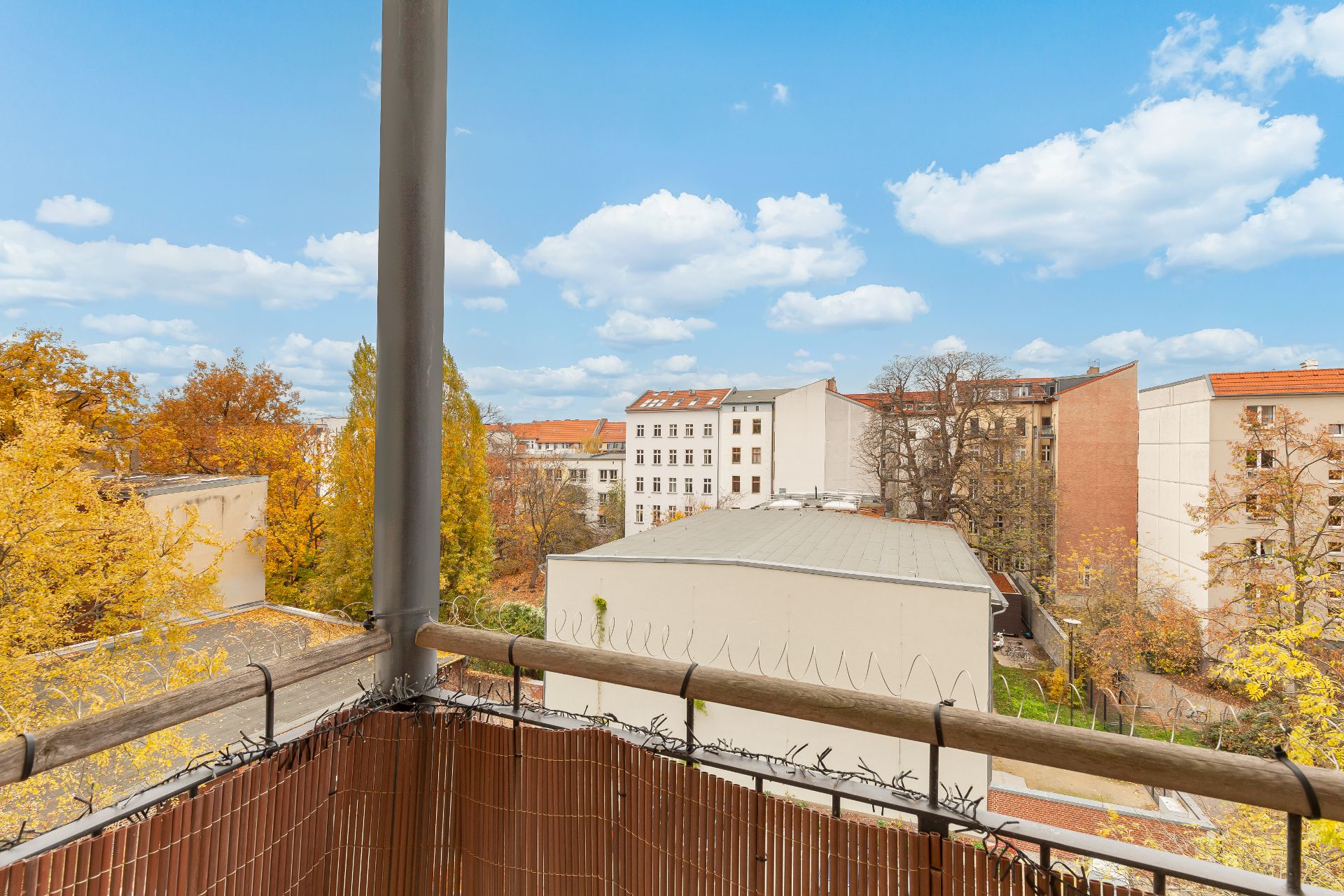 Blick von einem Balkon mit Bambusverkleidung auf Hinterhöfe und Bäume im Herbst.