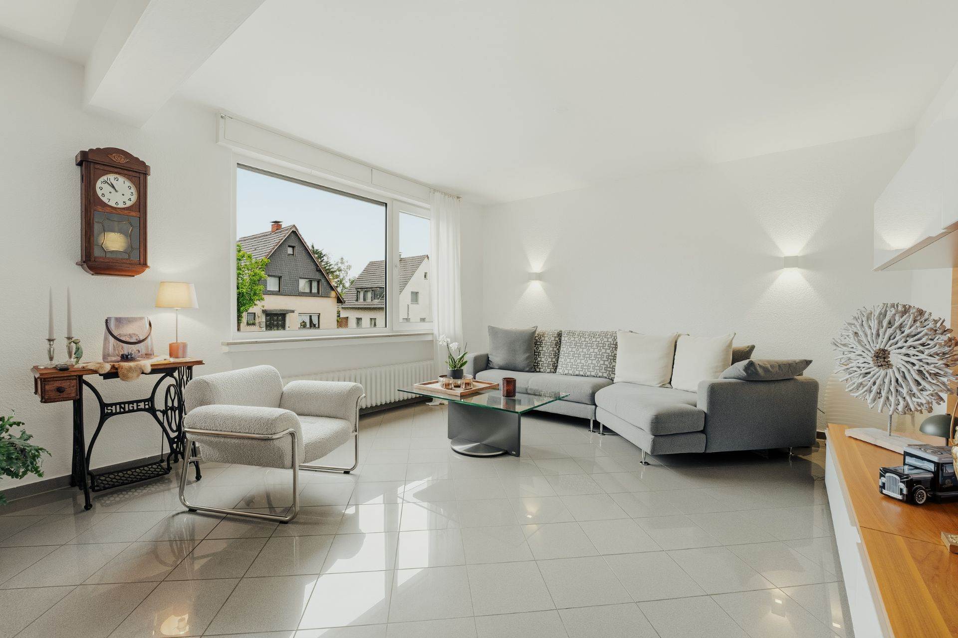 Helles Wohnzimmer mit Ecksofa, zwei Sesseln, Couchtisch und großem Fenster.