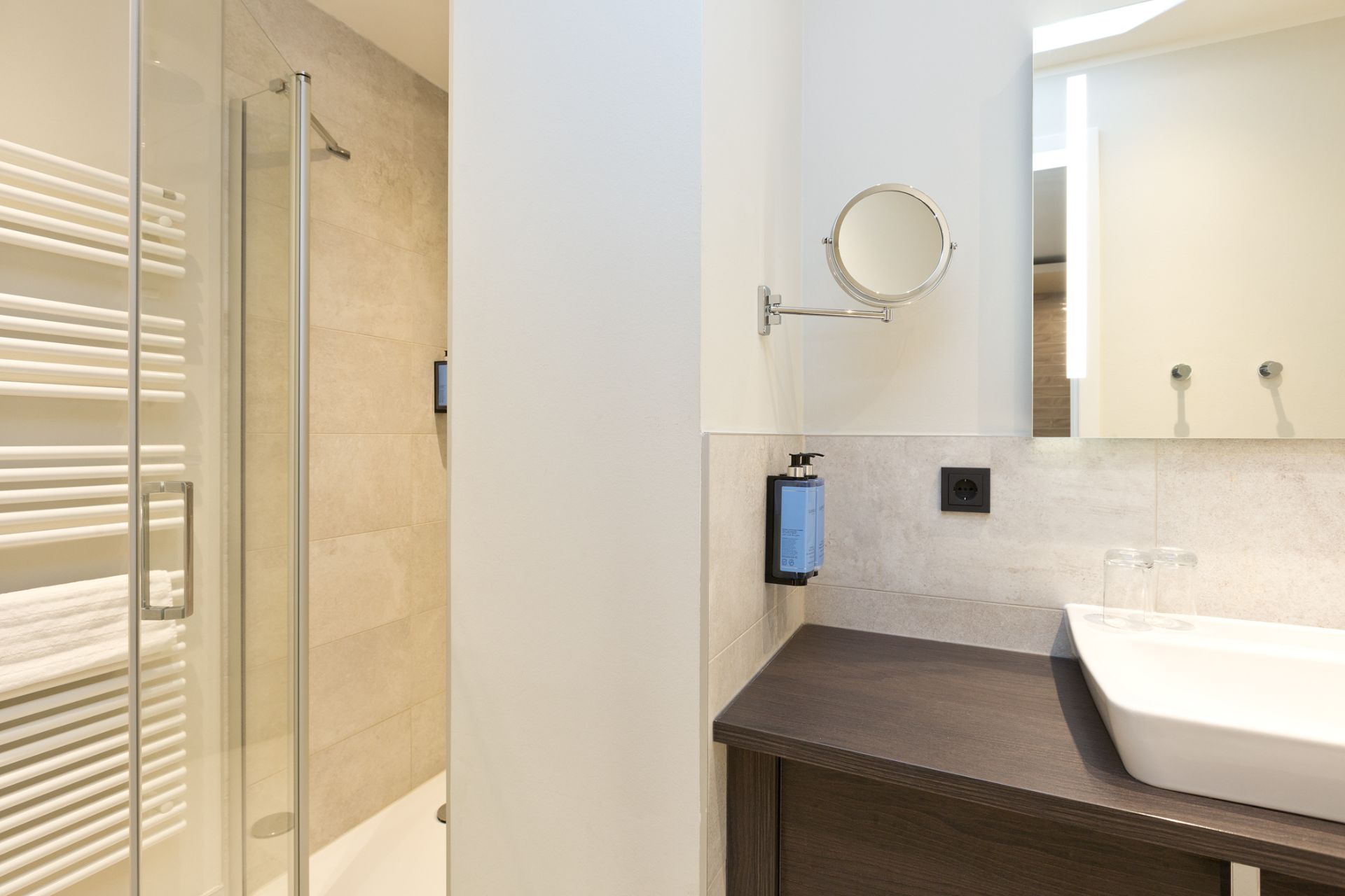 Modernes Badezimmer mit Dusche, Waschbecken, Spiegel und Handtuchheizkörper.
