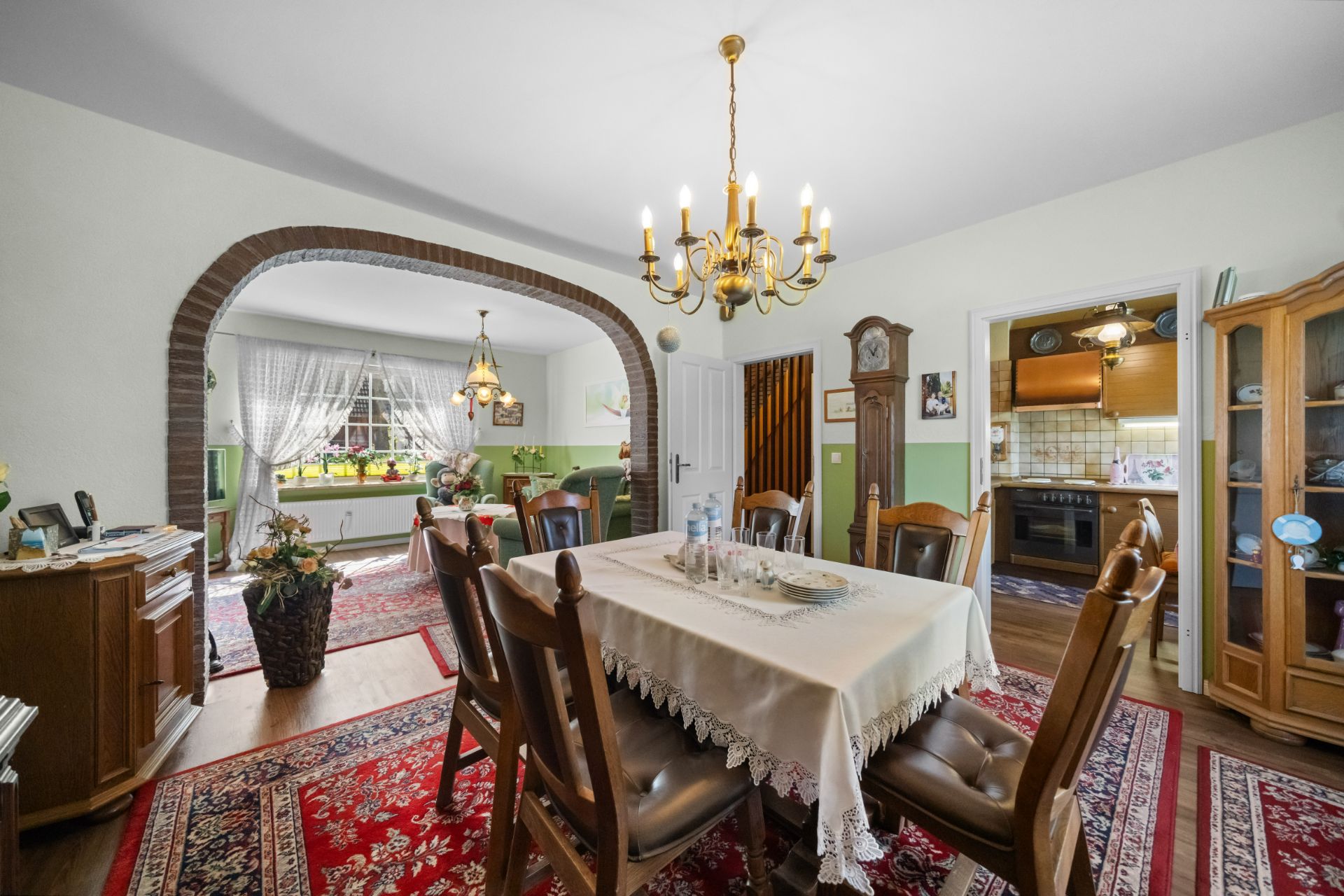 Esszimmer mit Holzmöbeln, Kronleuchter und Blick ins Wohnzimmer sowie in die Küche.