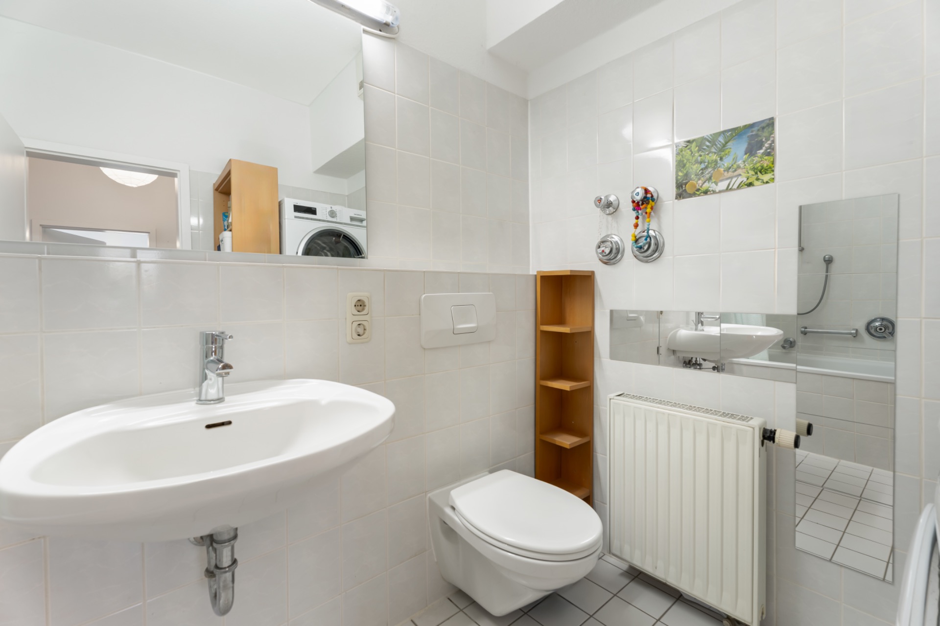 Helles Badezimmer mit Waschbecken, Toilette, Heizkörper, Spiegel und Regal.