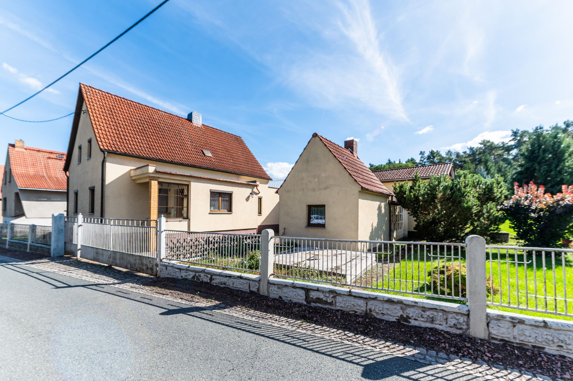 Einfamilienhaus mit rotem Dach, Vorgarten und Zaun an einer ruhigen Straße.