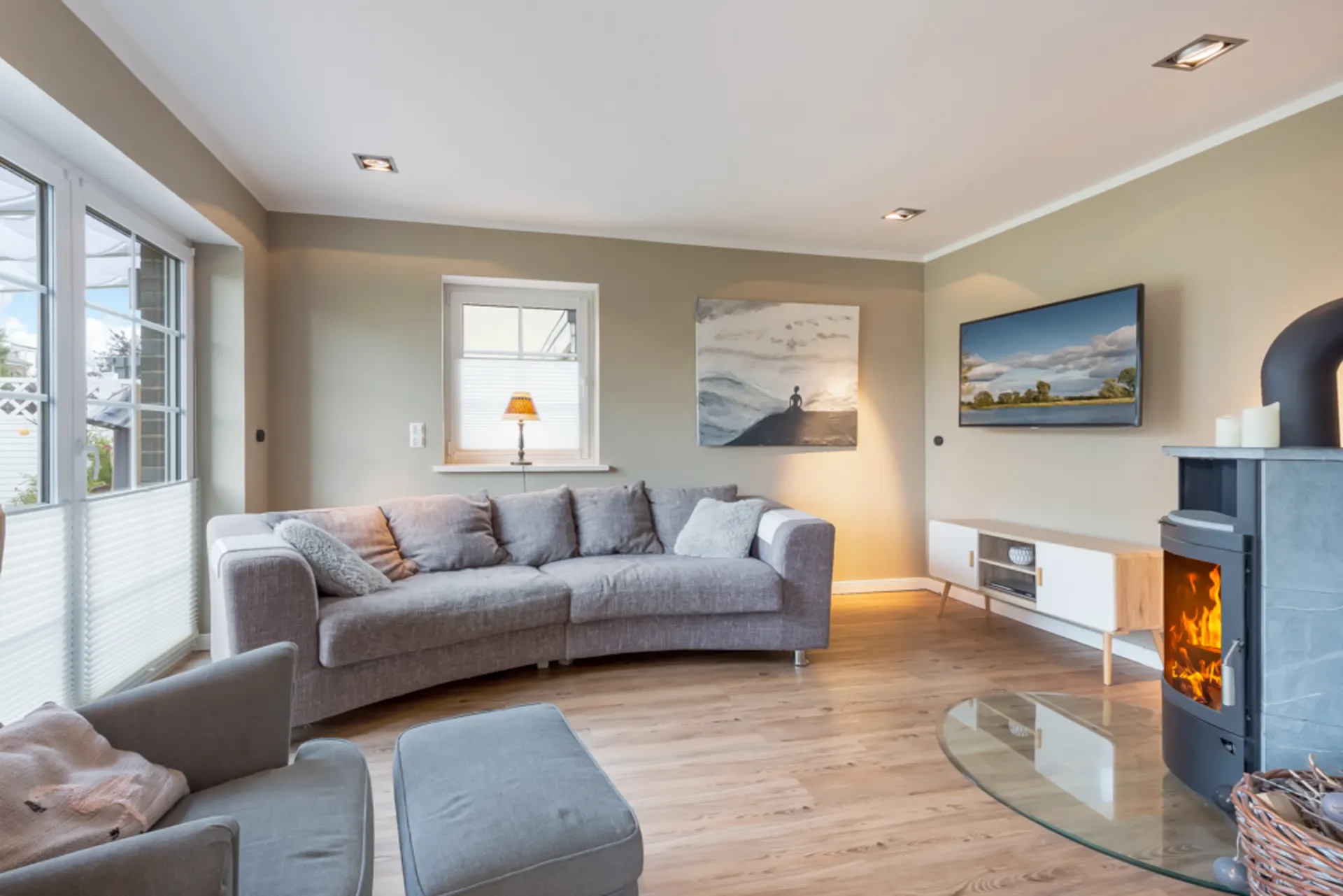 Modernes Wohnzimmer mit grauem Sofa, Sessel, Kamin, Fernseher und großem Fenster.