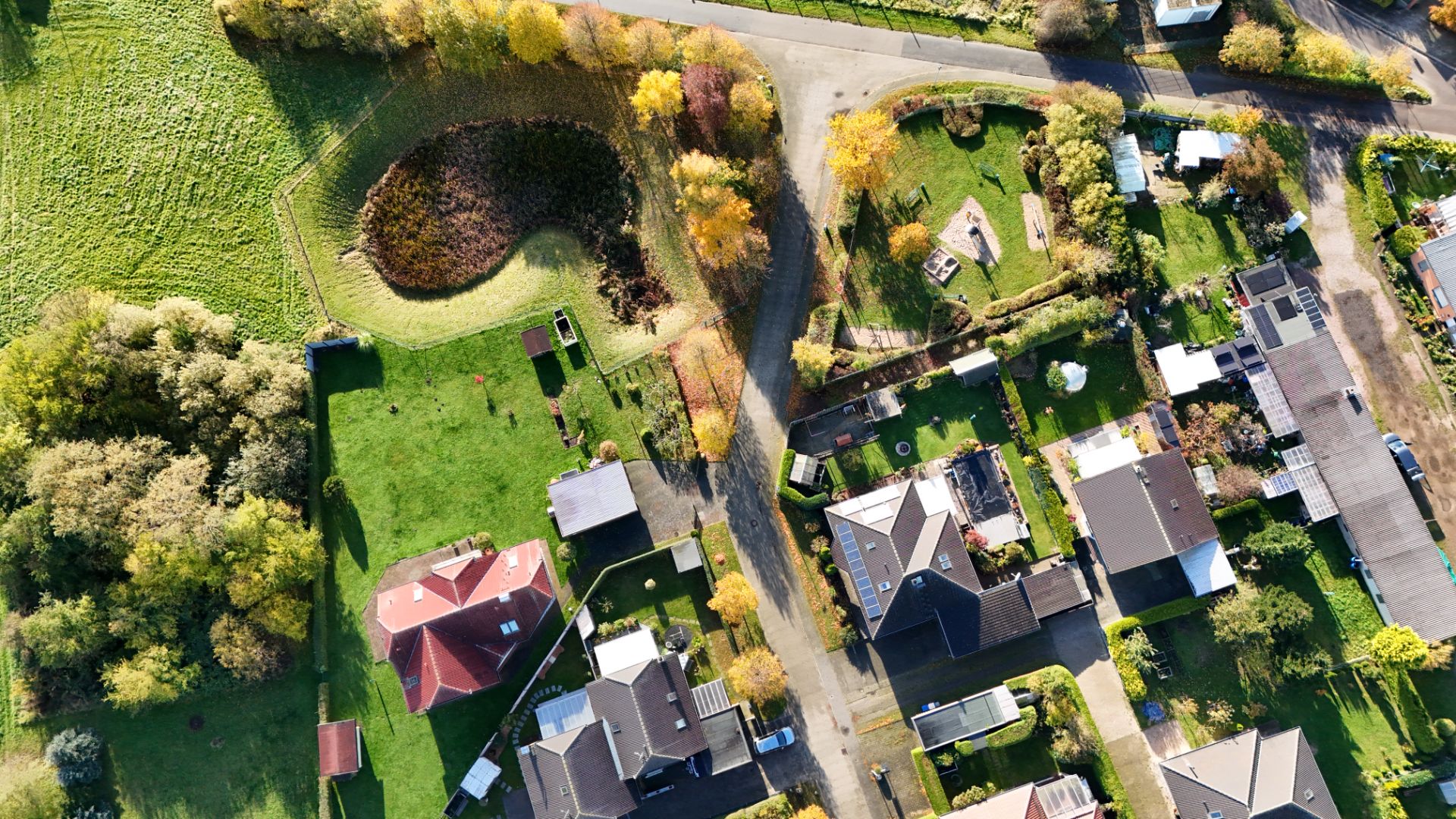Luftaufnahme von Wohnhäusern mit Gärten, Straße und Bäumen im Wohngebiet.
