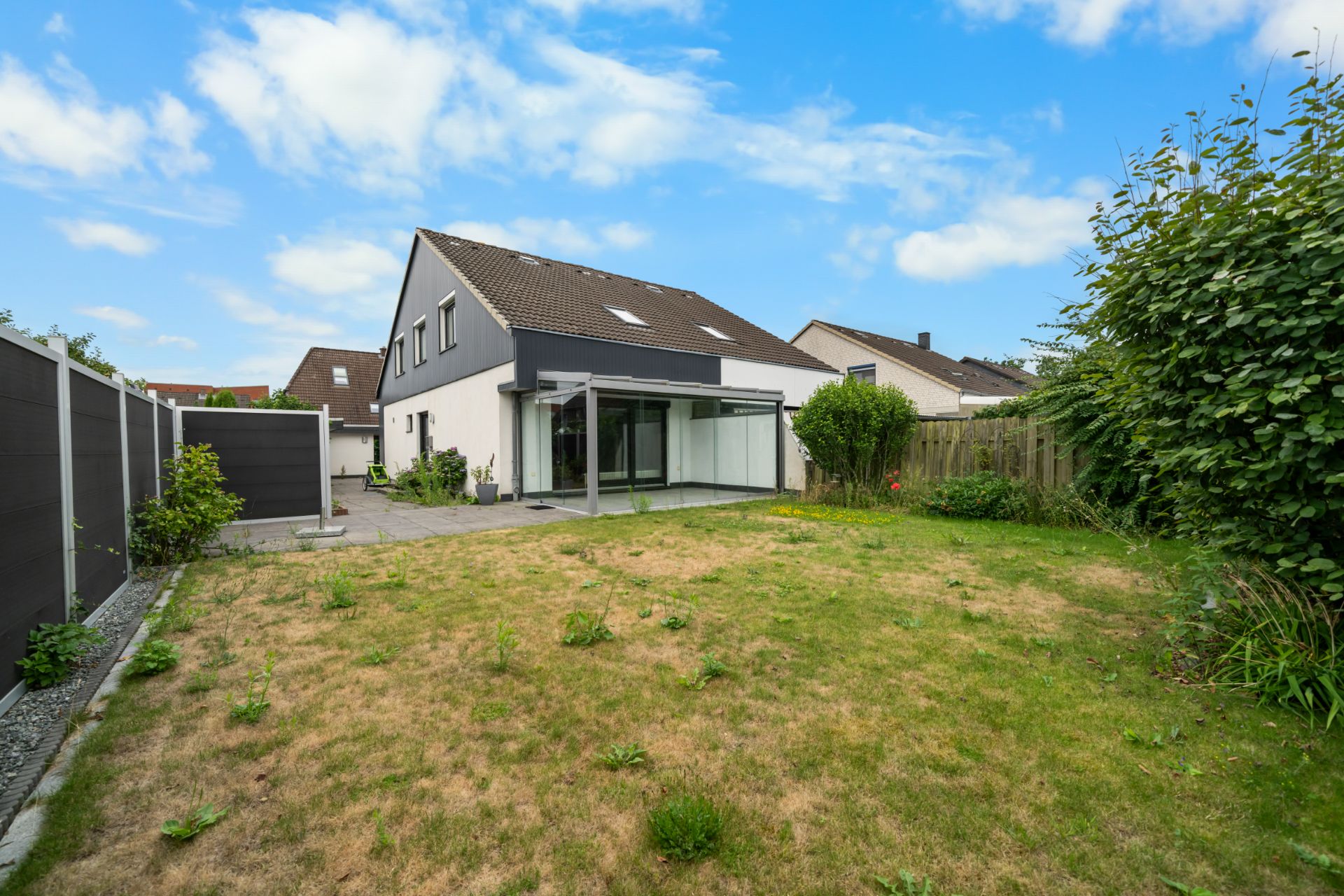 Rasenfläche mit Terrasse und modernem Einfamilienhaus im Hintergrund.