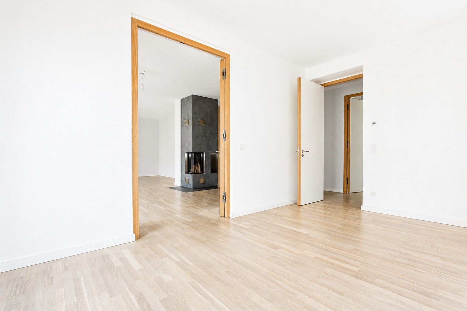 Leerer, heller Raum mit Holzboden, zwei offenen Türen und Kamin im Hintergrund.