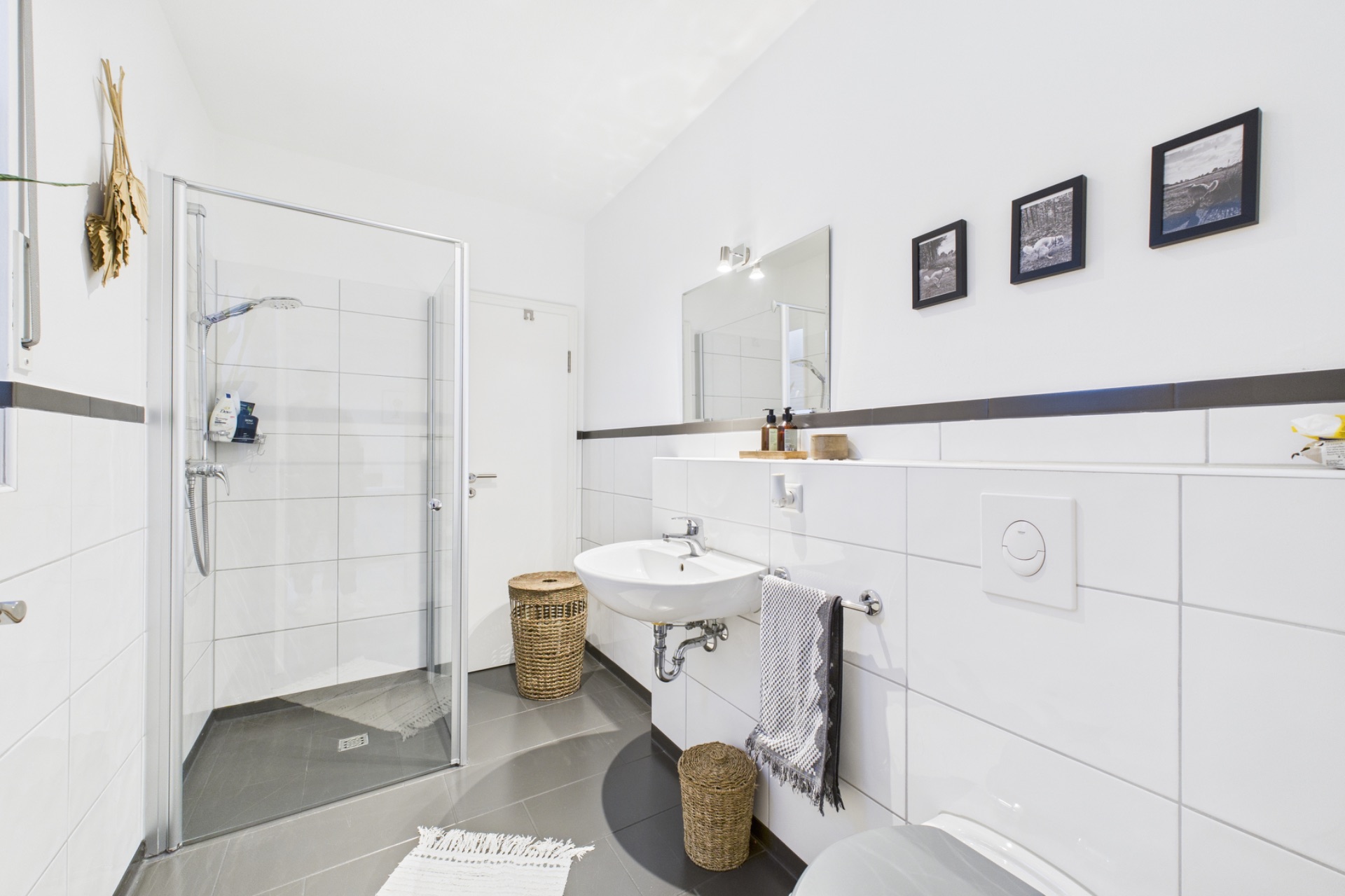 Modernes Bad mit bodengleicher Dusche, WC, Waschbecken, Spiegel und drei Wandbildern.