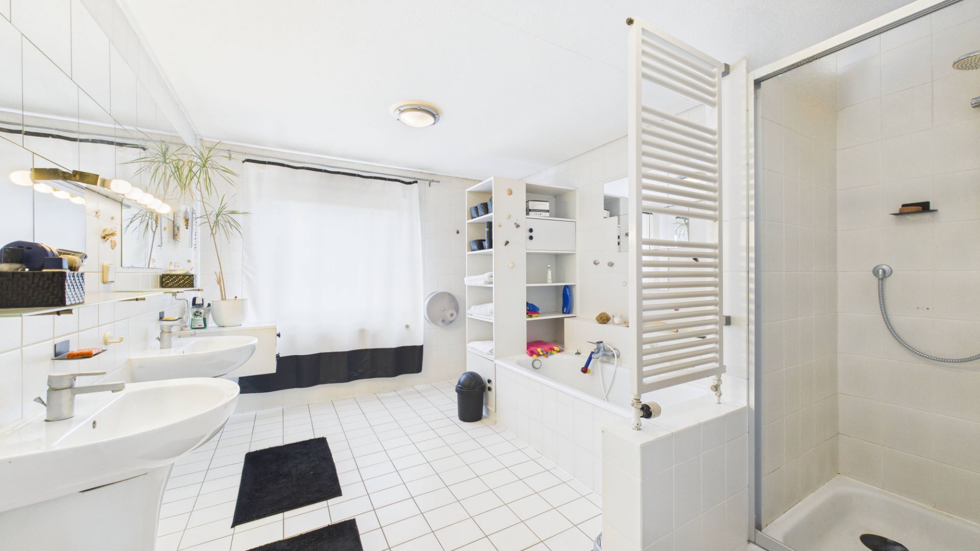 Helles Badezimmer mit Dusche, Badewanne, zwei Waschbecken und weißen Fliesen.