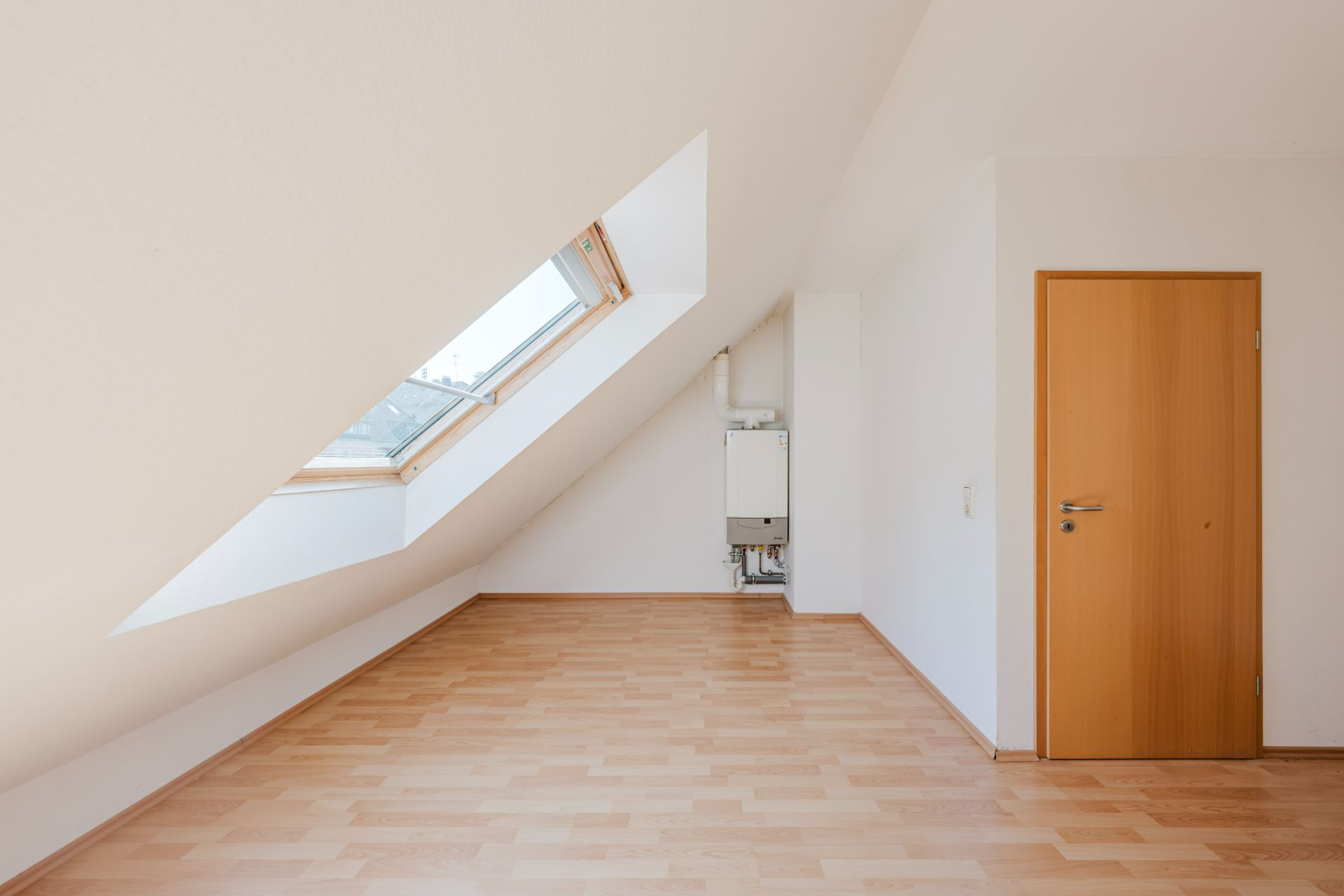 Heller Raum mit Dachschräge, großem Dachfenster, Holzfußboden und Holztür.