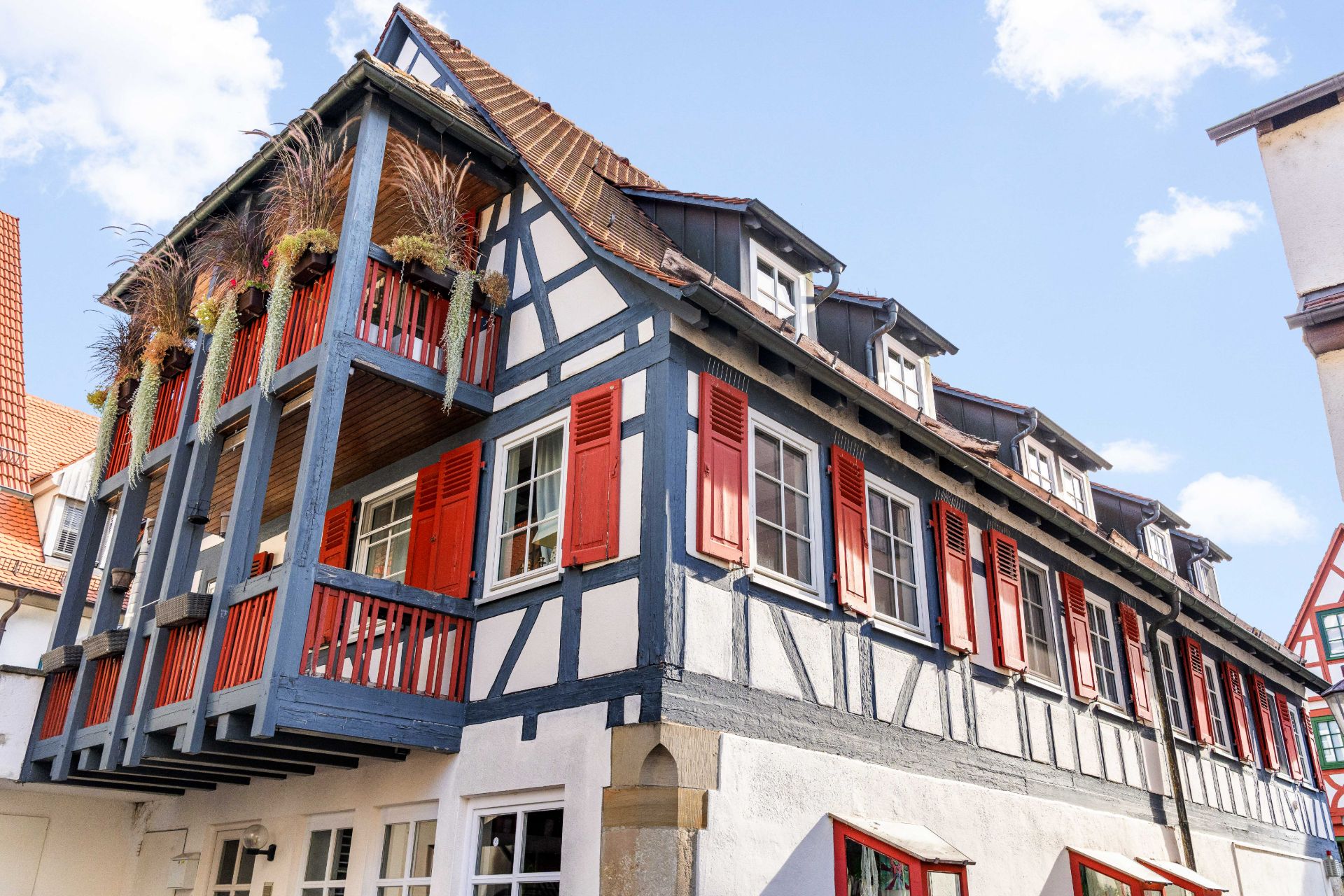 Fachwerkhaus mit roten Fensterläden und Balkon mit Pflanzen, aufgenommen bei Tageslicht.