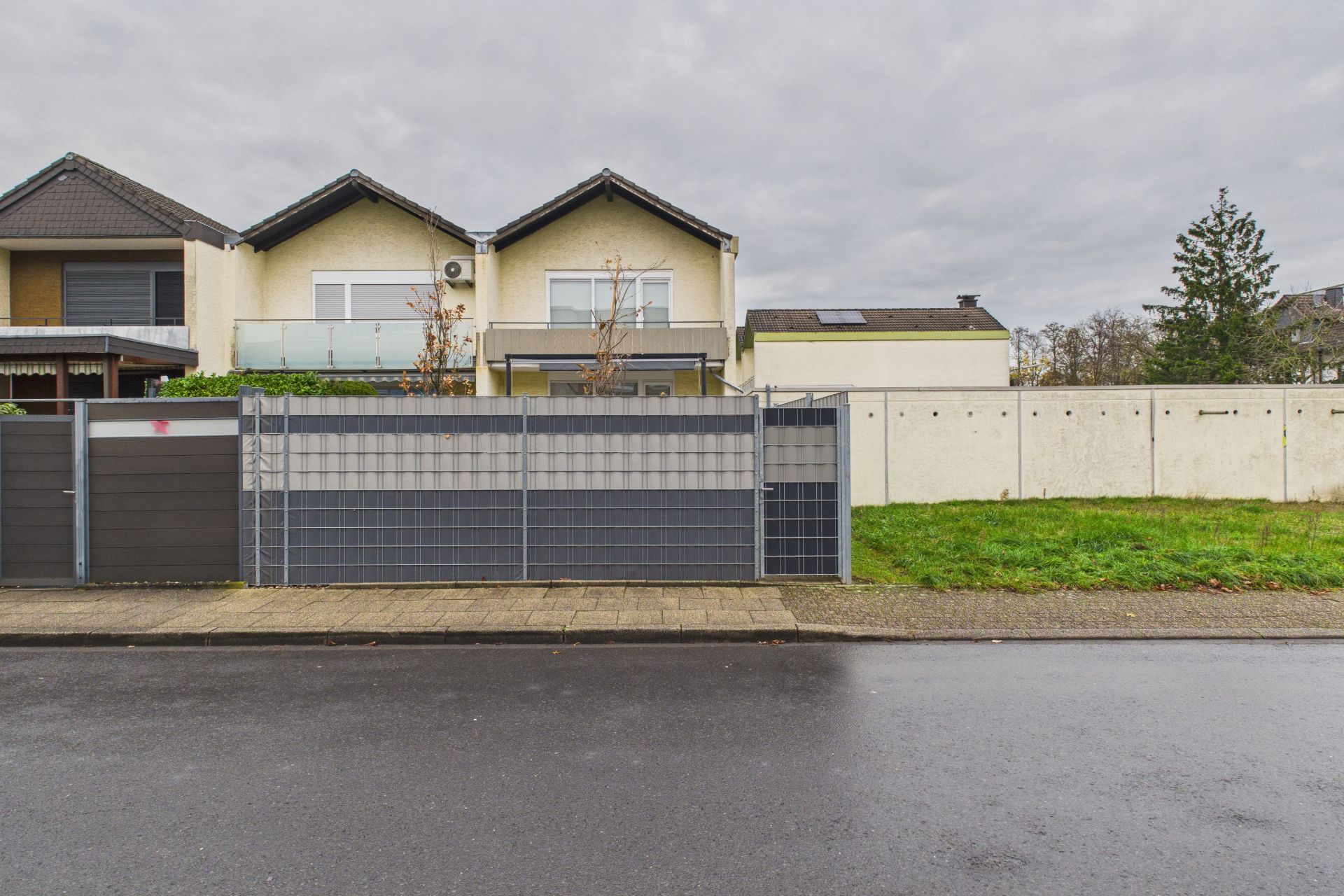 Zweistöckiges Wohnhaus mit Balkon, modernem Zaun und Vorgarten, aufgenommen von der Straße.