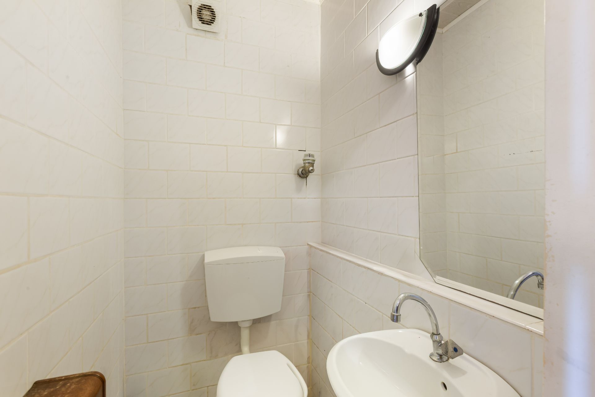 Kleines Badezimmer mit Toilette, Waschbecken, Spiegel und weiß gefliesten Wänden.
