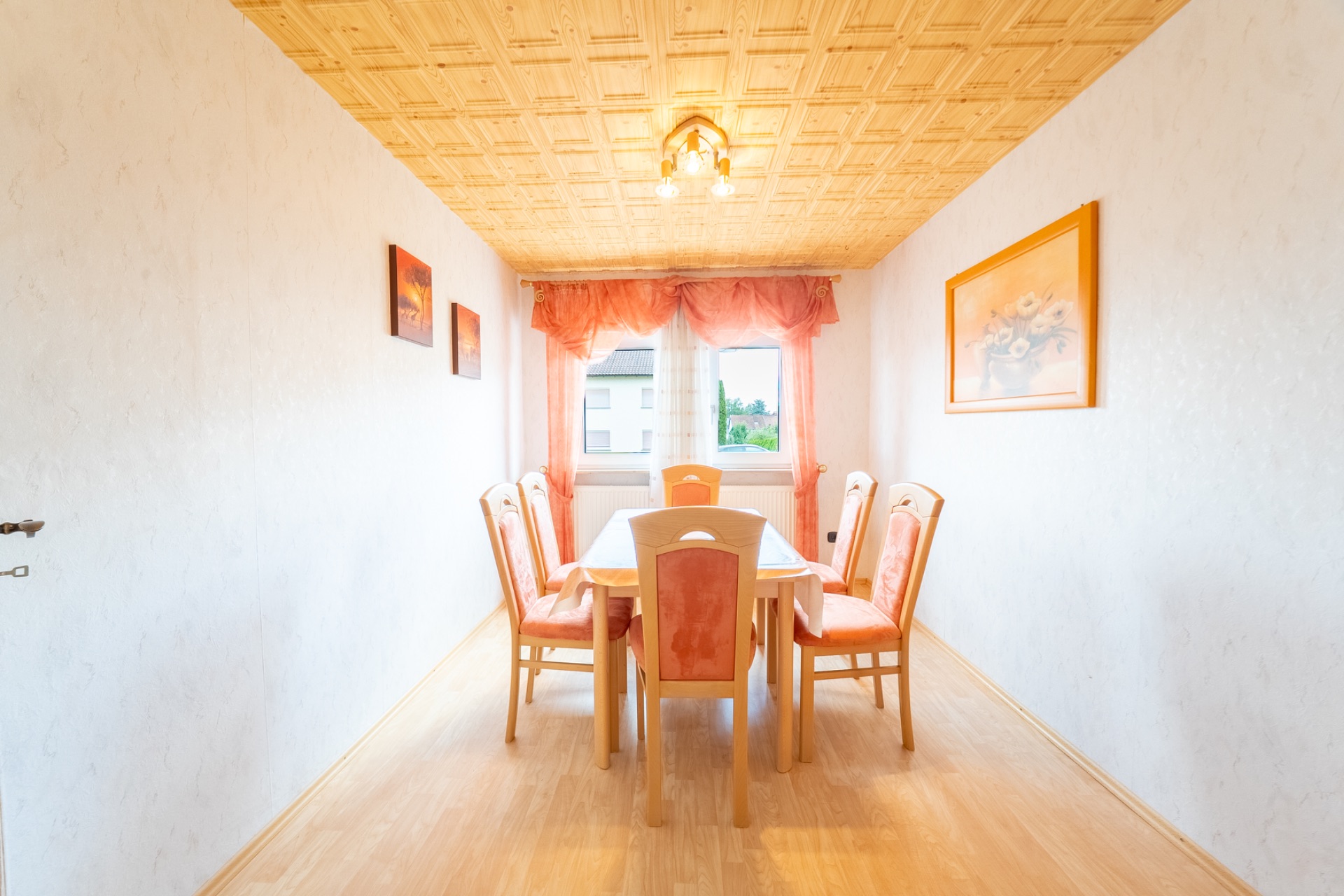 Helles Esszimmer mit Holztisch, sechs Stühlen, Fenster und Bildern an den Wänden.