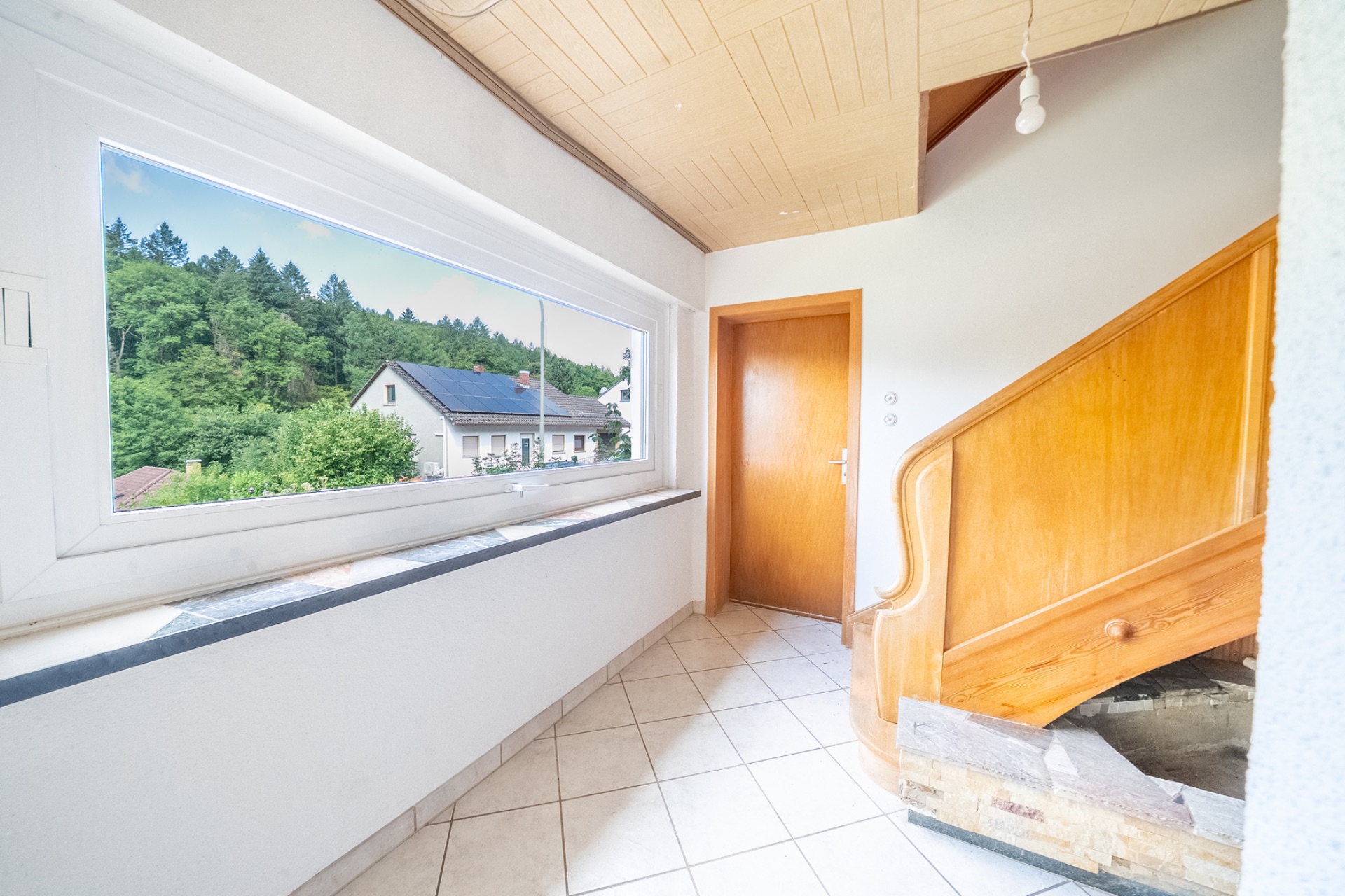 Heller Flur mit großem Fenster, Holztür und Treppe mit Holzgeländer.