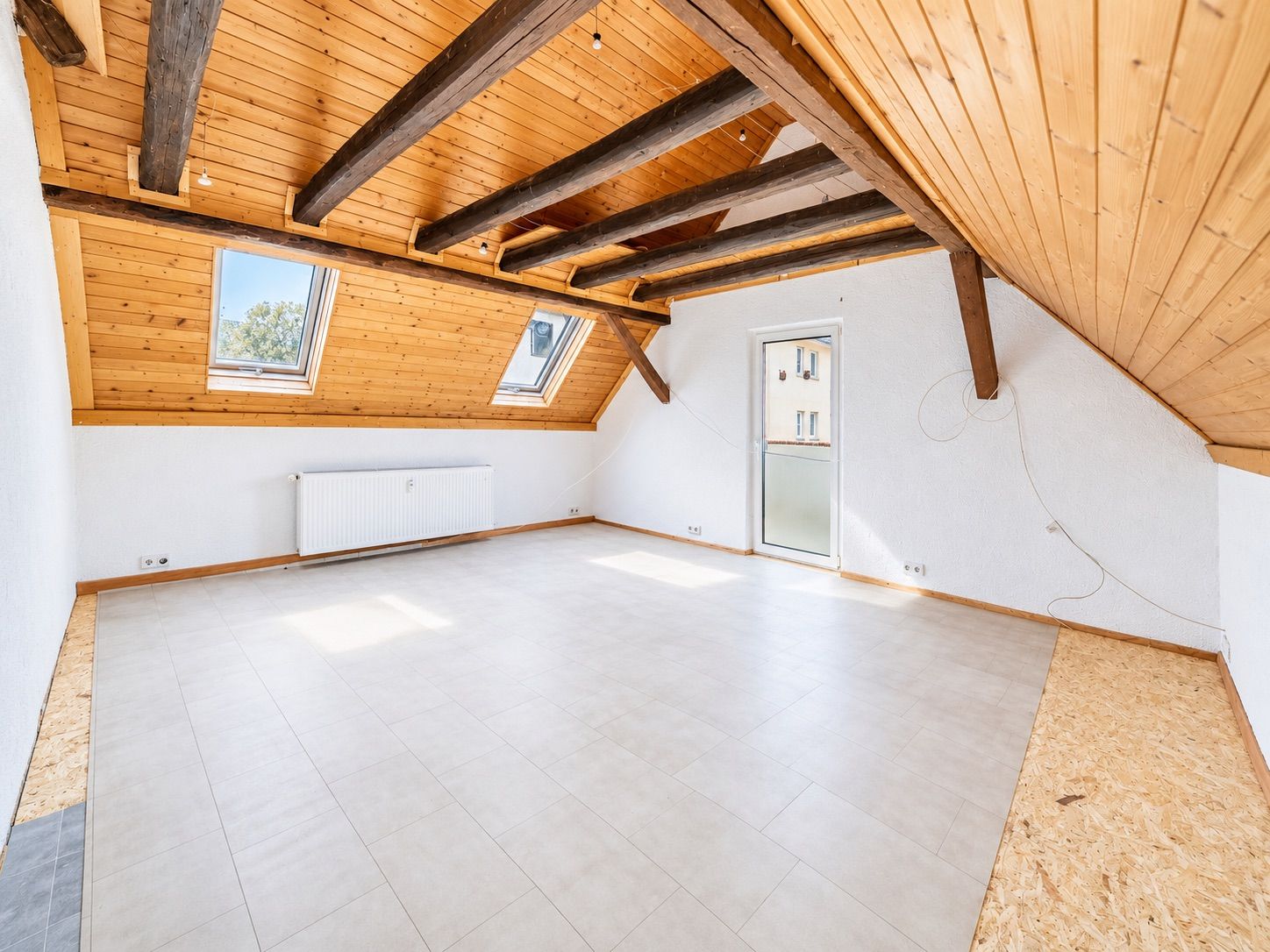 Heller Dachraum mit Holzdecke, freiliegenden Balken, zwei Dachfenstern und weißem Boden.