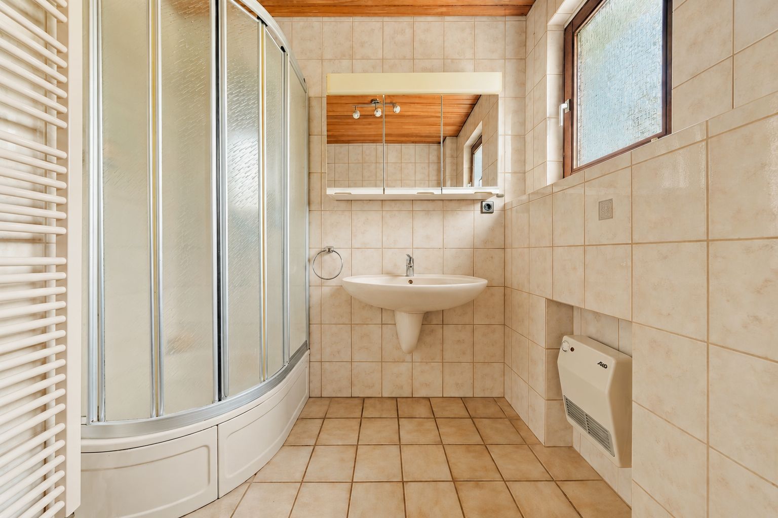 Helles Bad mit Eckdusche, Waschbecken, Spiegel und Fenster, Wände und Boden sind gefliest.