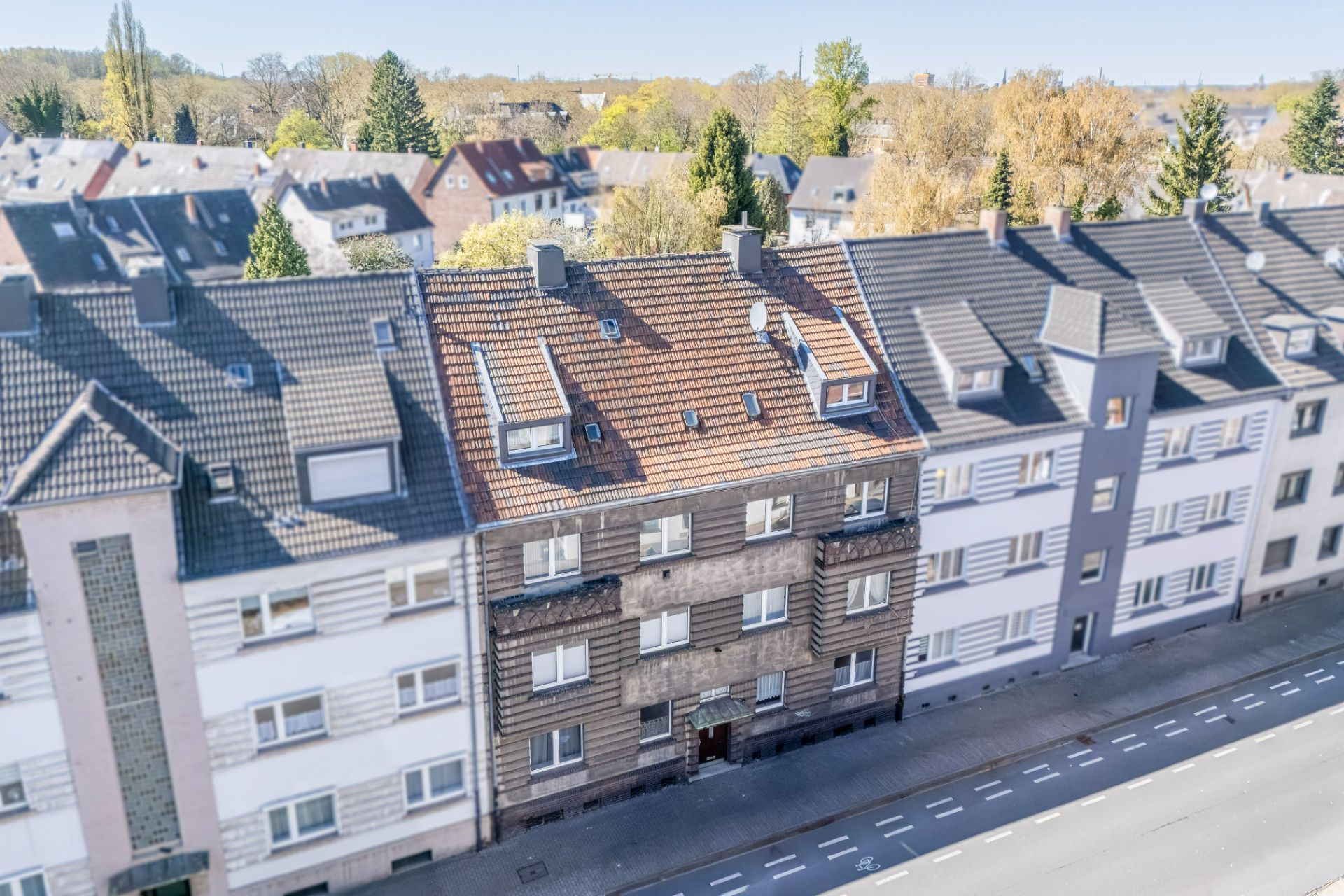 Mehrstöckiges Wohnhaus mit brauner Fassade und Ziegeldach an einer Straße.