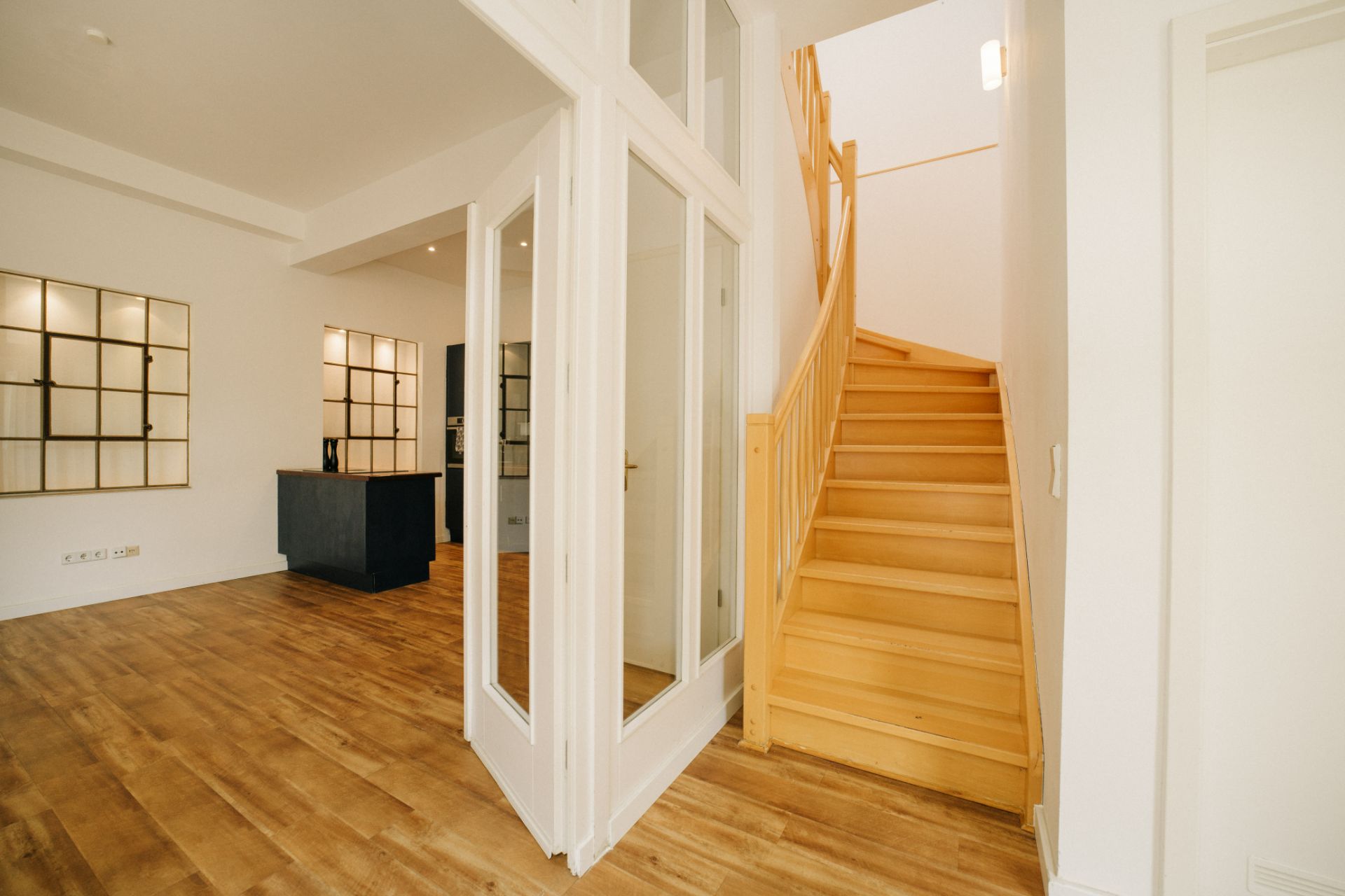 Heller Flur mit Holzboden, Glastüren und einer Holztreppe nach oben.