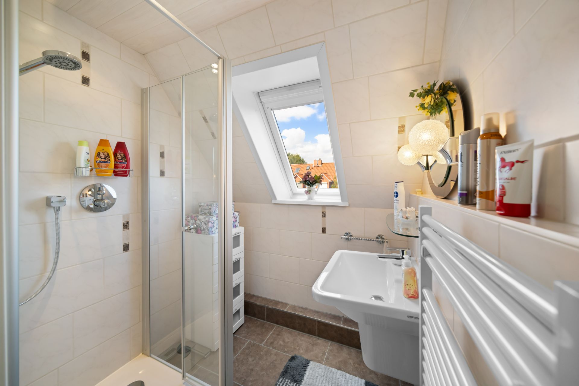 Helles Badezimmer mit Dusche, Waschbecken, Fenster und Handtuchheizung.