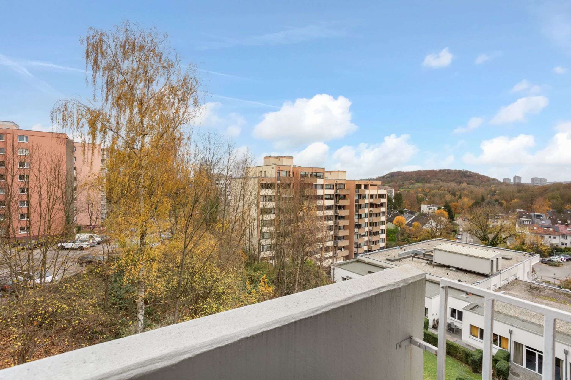 Blick von einem Balkon auf Wohngebäude, Bäume und einen Hügel im Hintergrund.