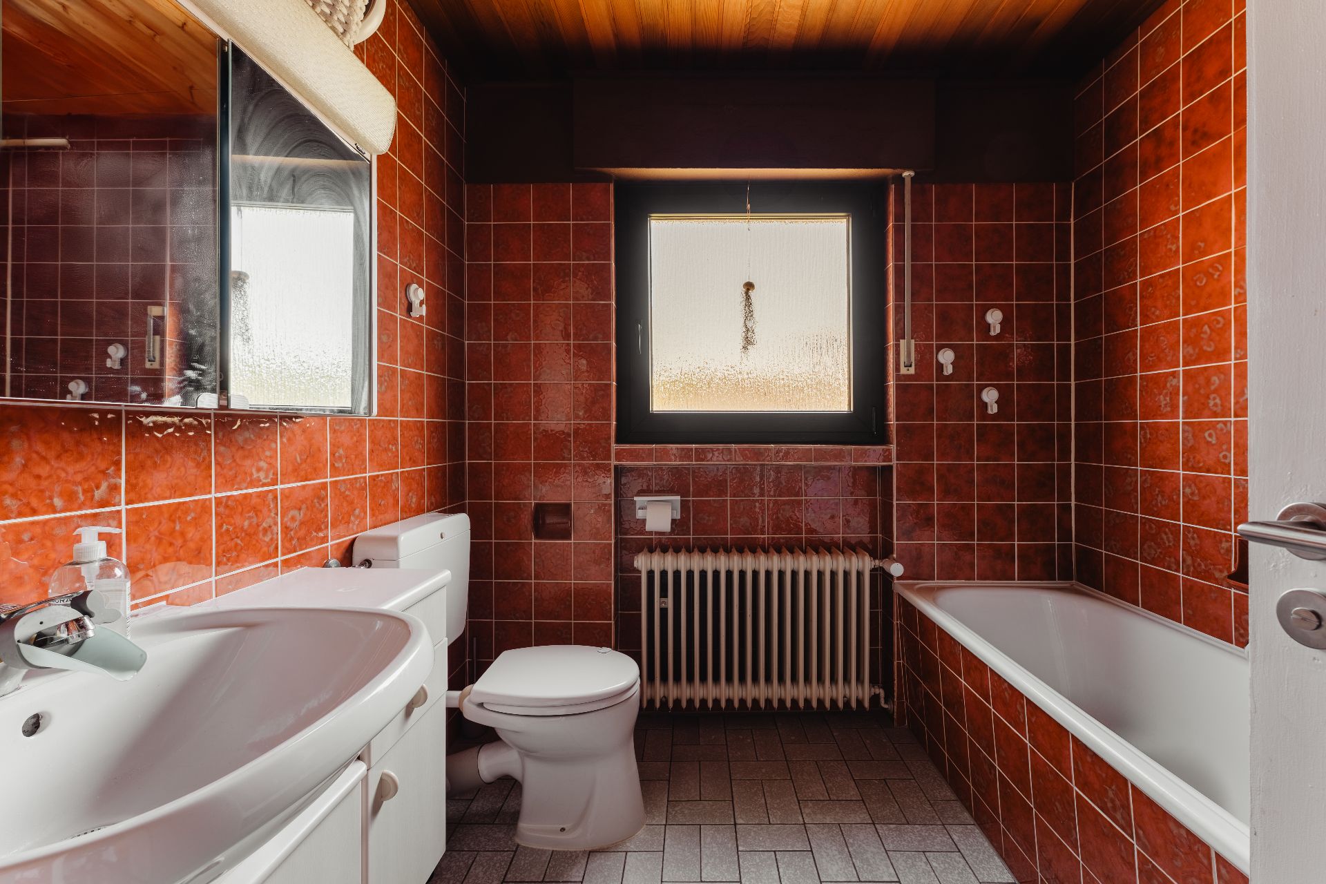 Badezimmer mit rotem Fliesenspiegel, Waschbecken, Toilette, Badewanne und Fenster.