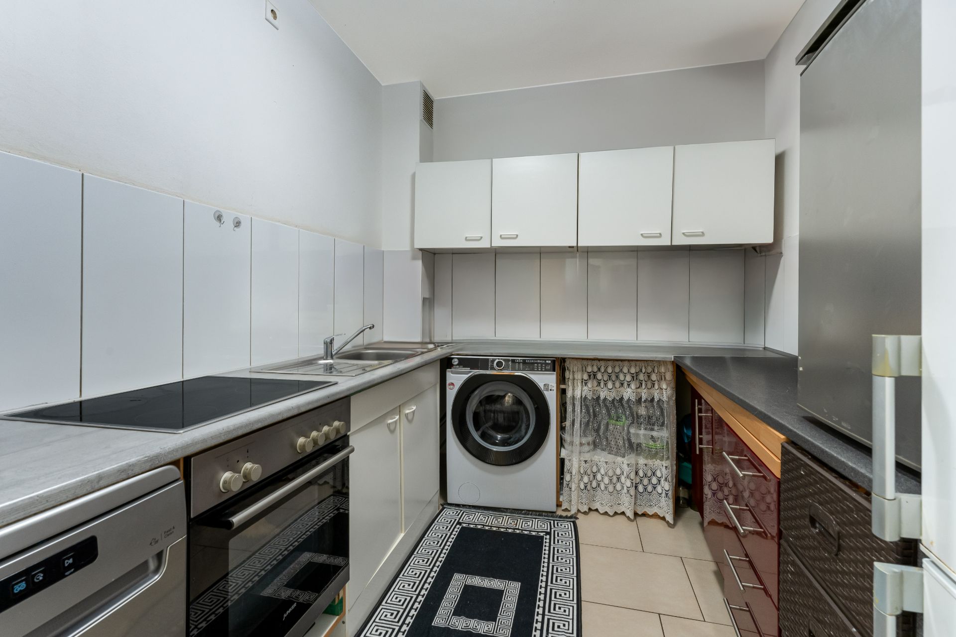 Moderne Küche mit Herd, Ofen, Waschmaschine, Spülmaschine, weißen Schränken und Teppich.