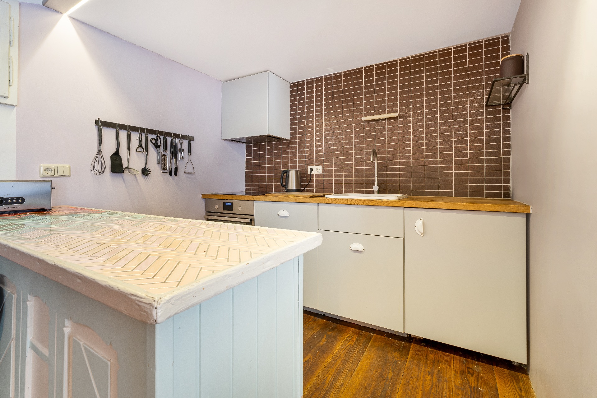 Küche mit brauner Fliesenwand, Holzarbeitsplatte und Küchenutensilien an der Wand.