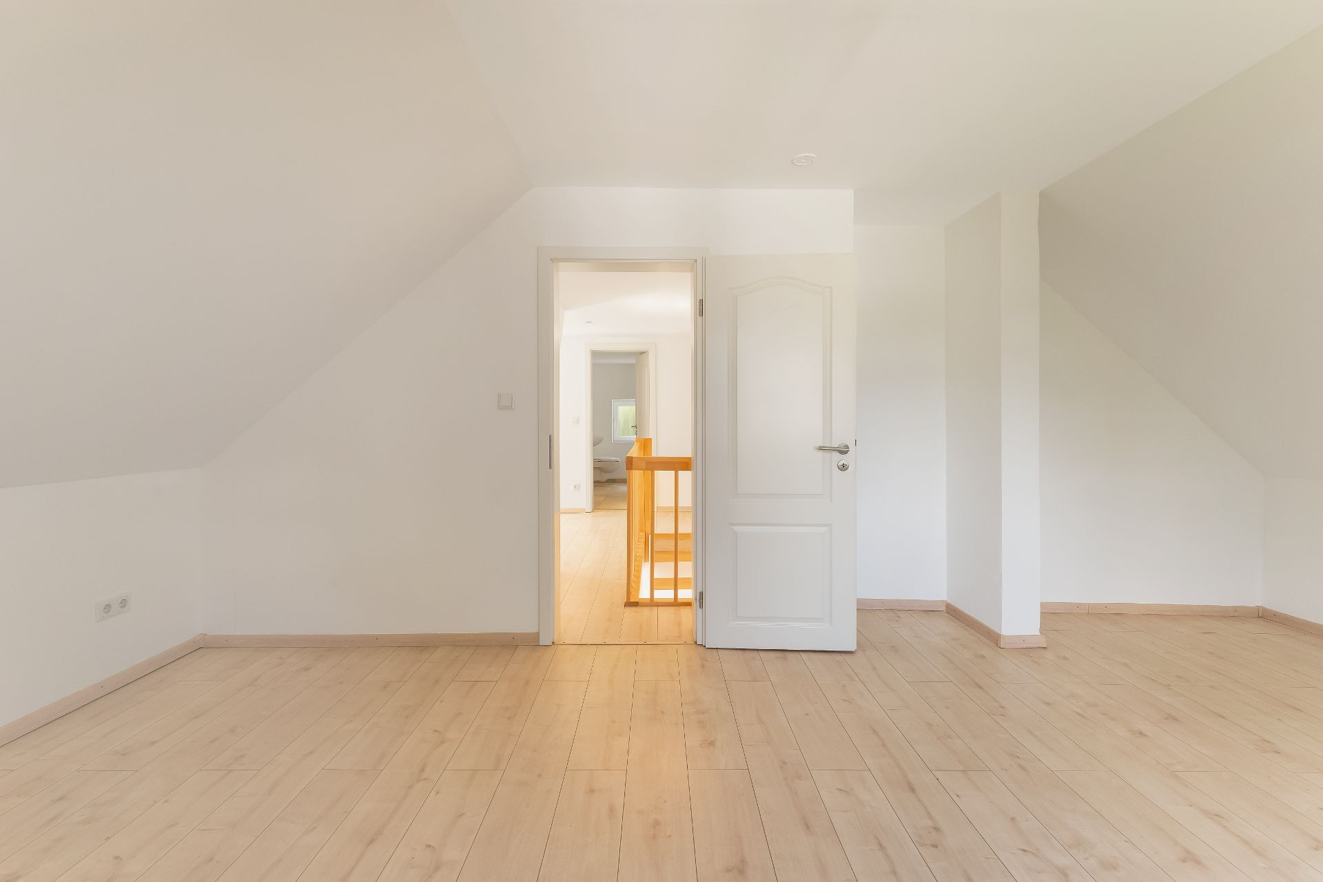 Leeres Zimmer mit Holzfußboden und offener Tür, Blick auf Flur und Treppe.