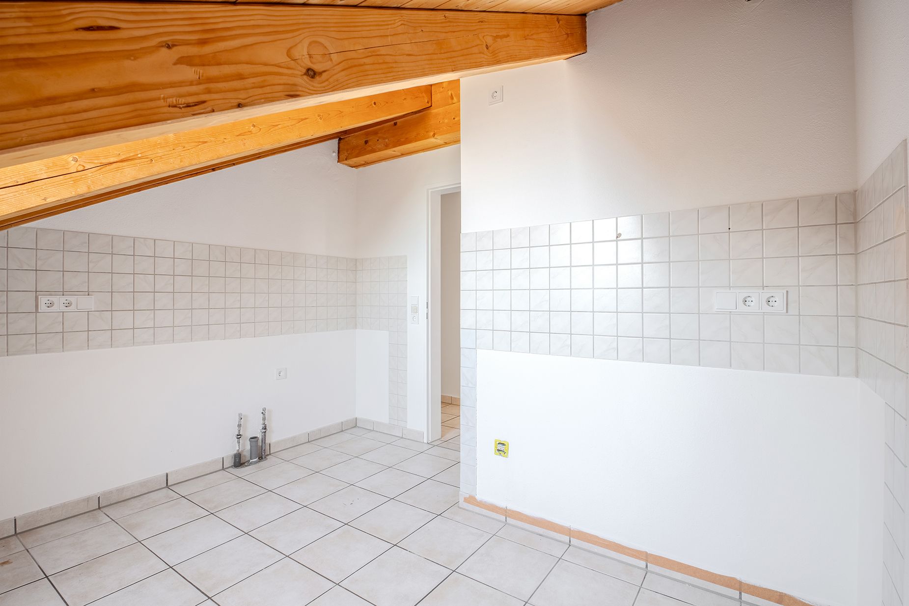 Leerer Raum mit Fliesenspiegel, weißen Wänden und sichtbaren Holzbalken unter der Schräge.