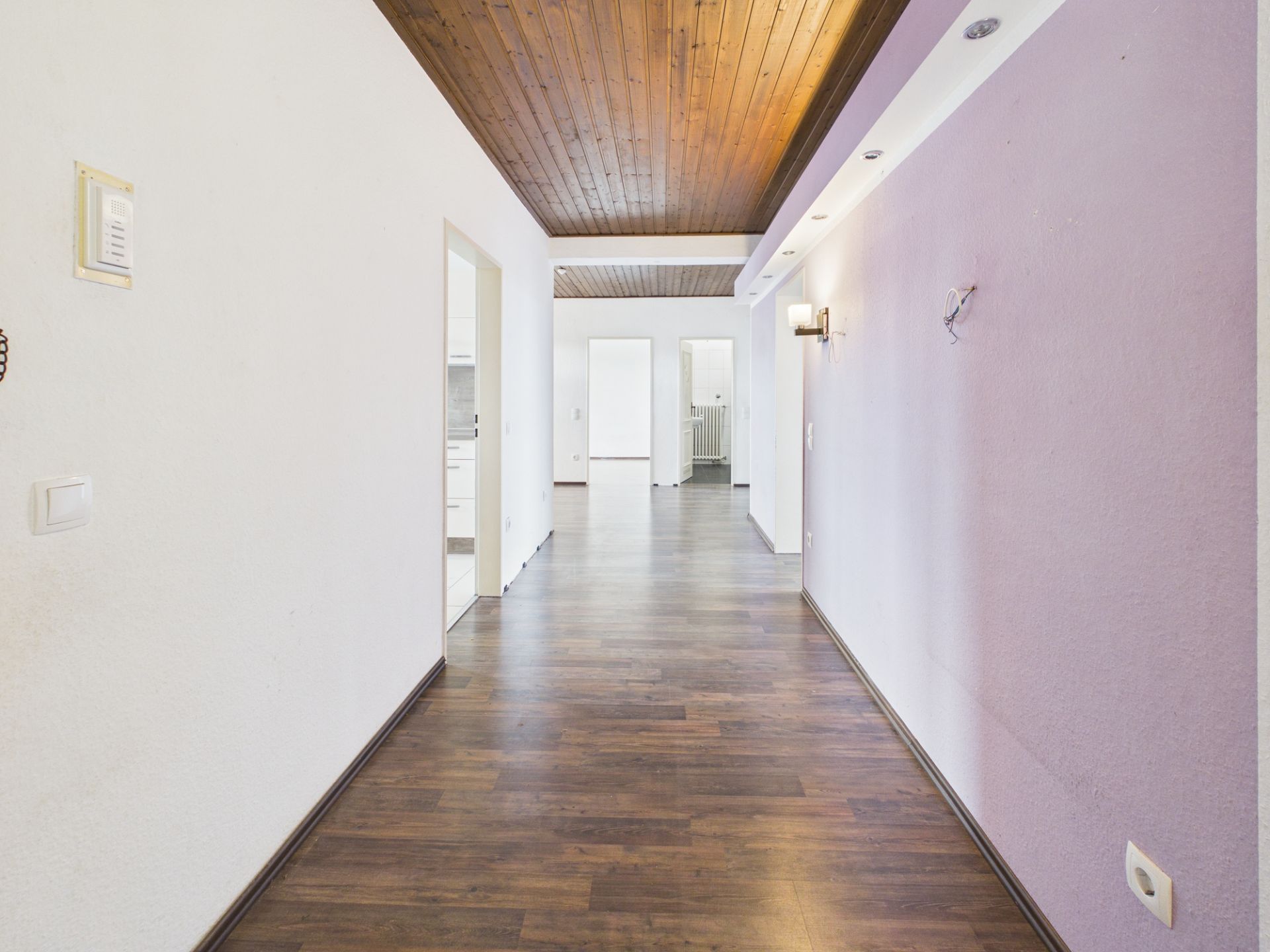 Heller Flur mit Holzdecke, Laminatboden und lila Wand, Türen zu weiteren Zimmern.