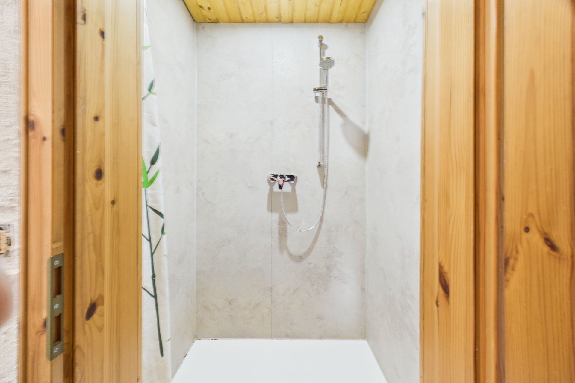 Dusche mit hellen Fliesen, Holztürrahmen und Duschvorhang mit Pflanzenmotiv.