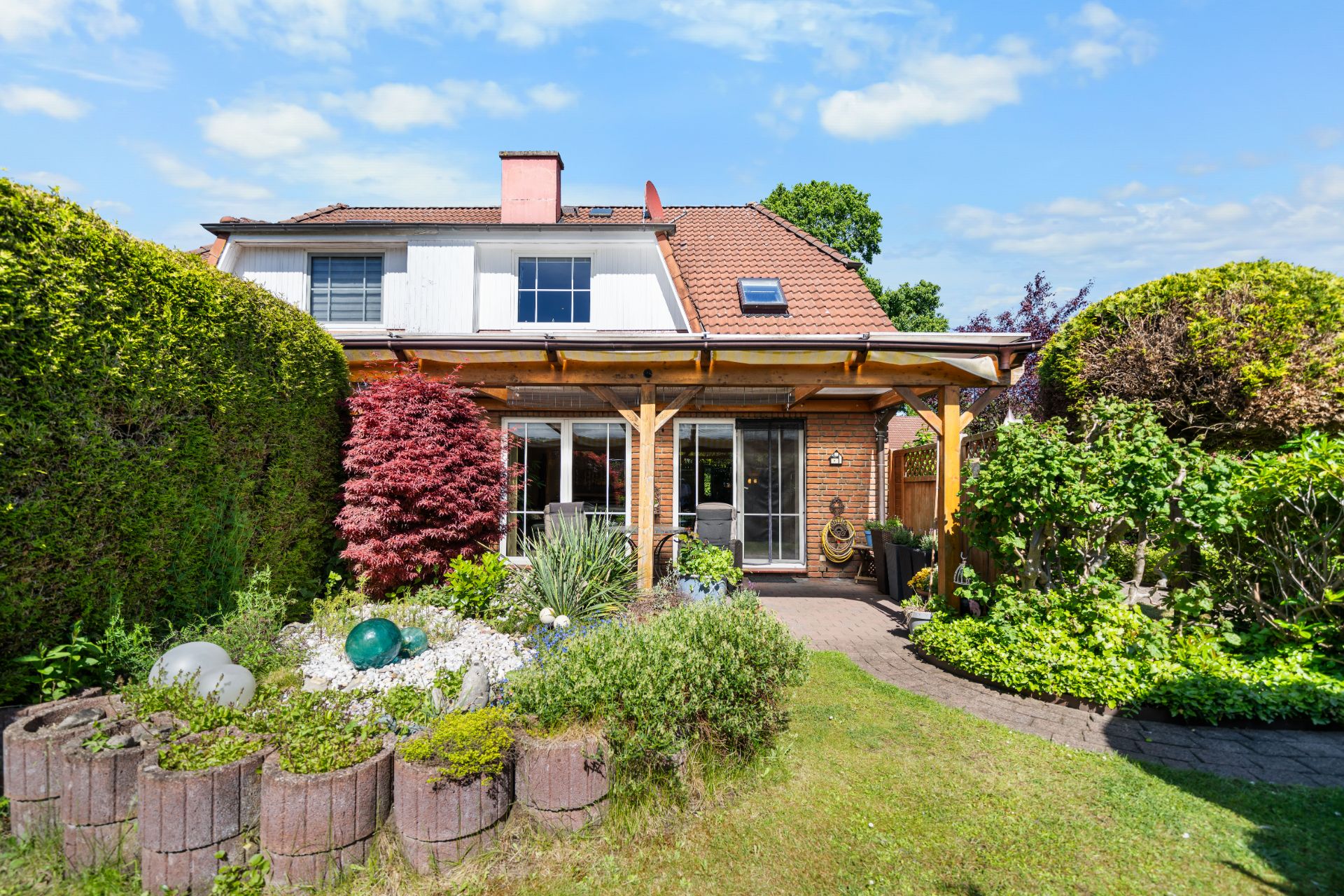 Gepflegter Garten mit überdachter Terrasse vor einem Einfamilienhaus mit rotem Dach.