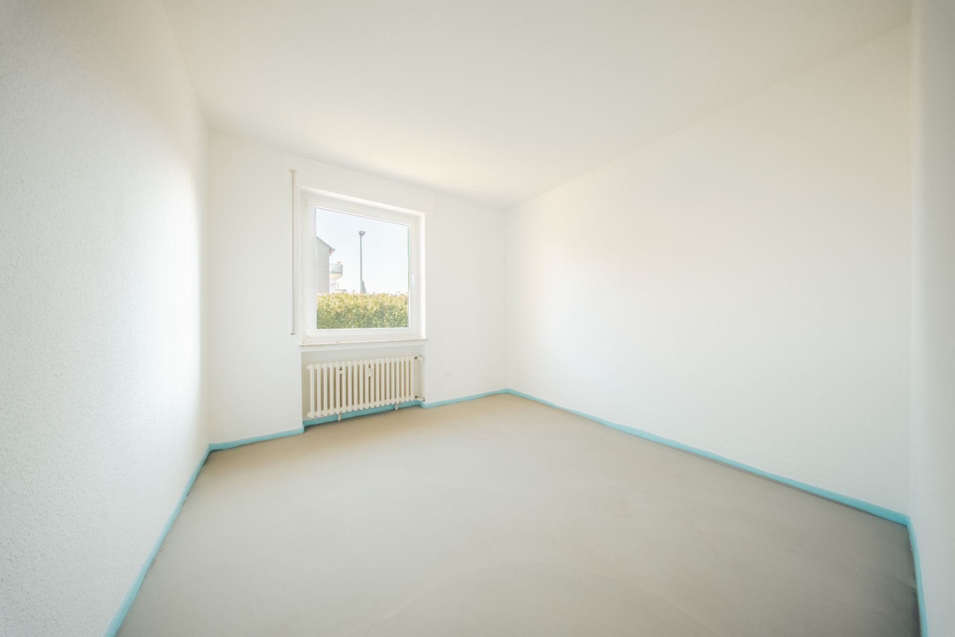 Leerer, heller Raum mit weiß gestrichenen Wänden, Fenster und Heizkörper unter dem Fenster.