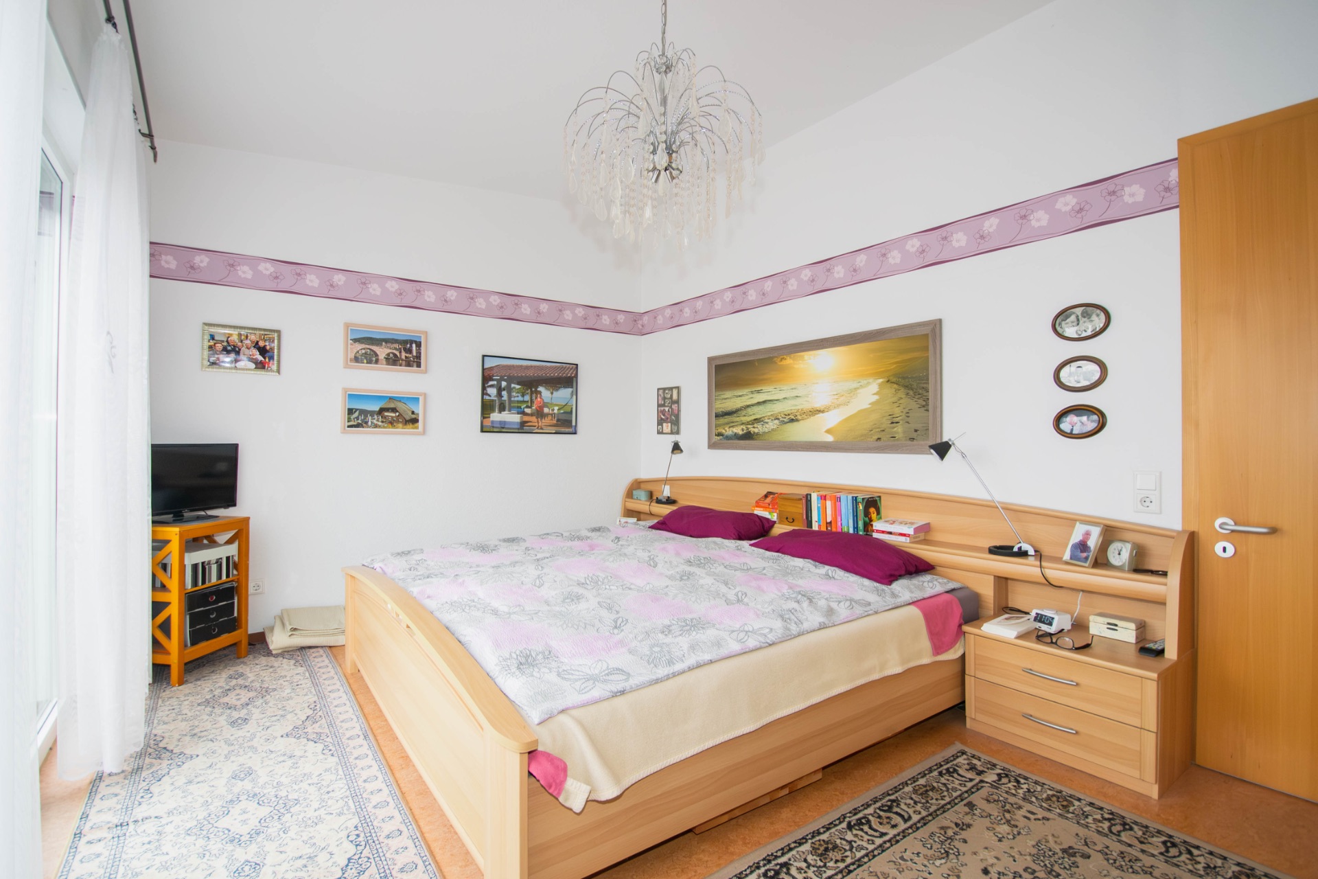 Helles Schlafzimmer mit Doppelbett, Nachttischen, Teppich und Bildern an der Wand.