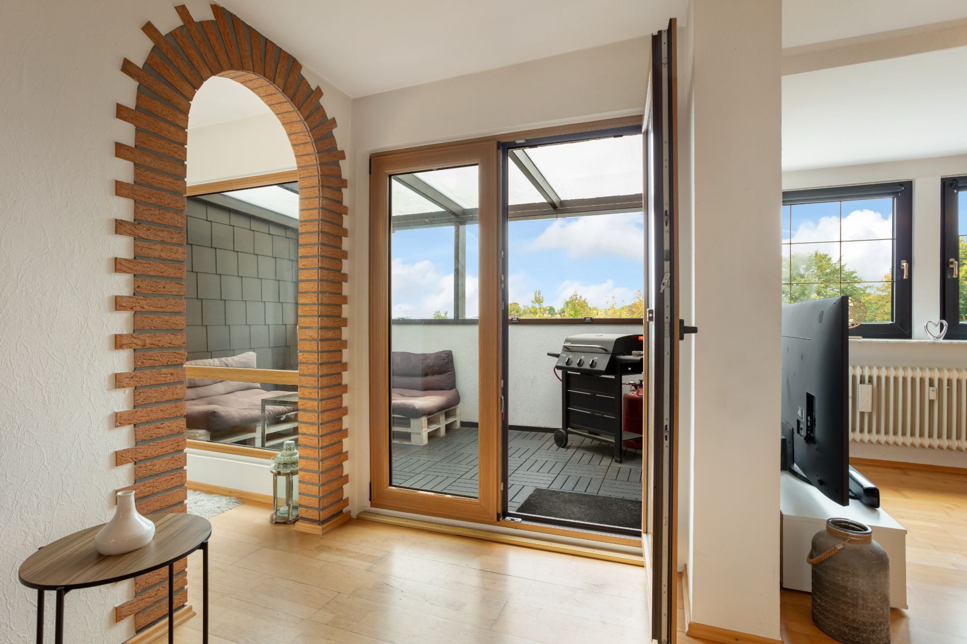 Wohnbereich mit bogenförmigem Durchgang und Zugang zum Balkon mit Grill und Sitzbank.