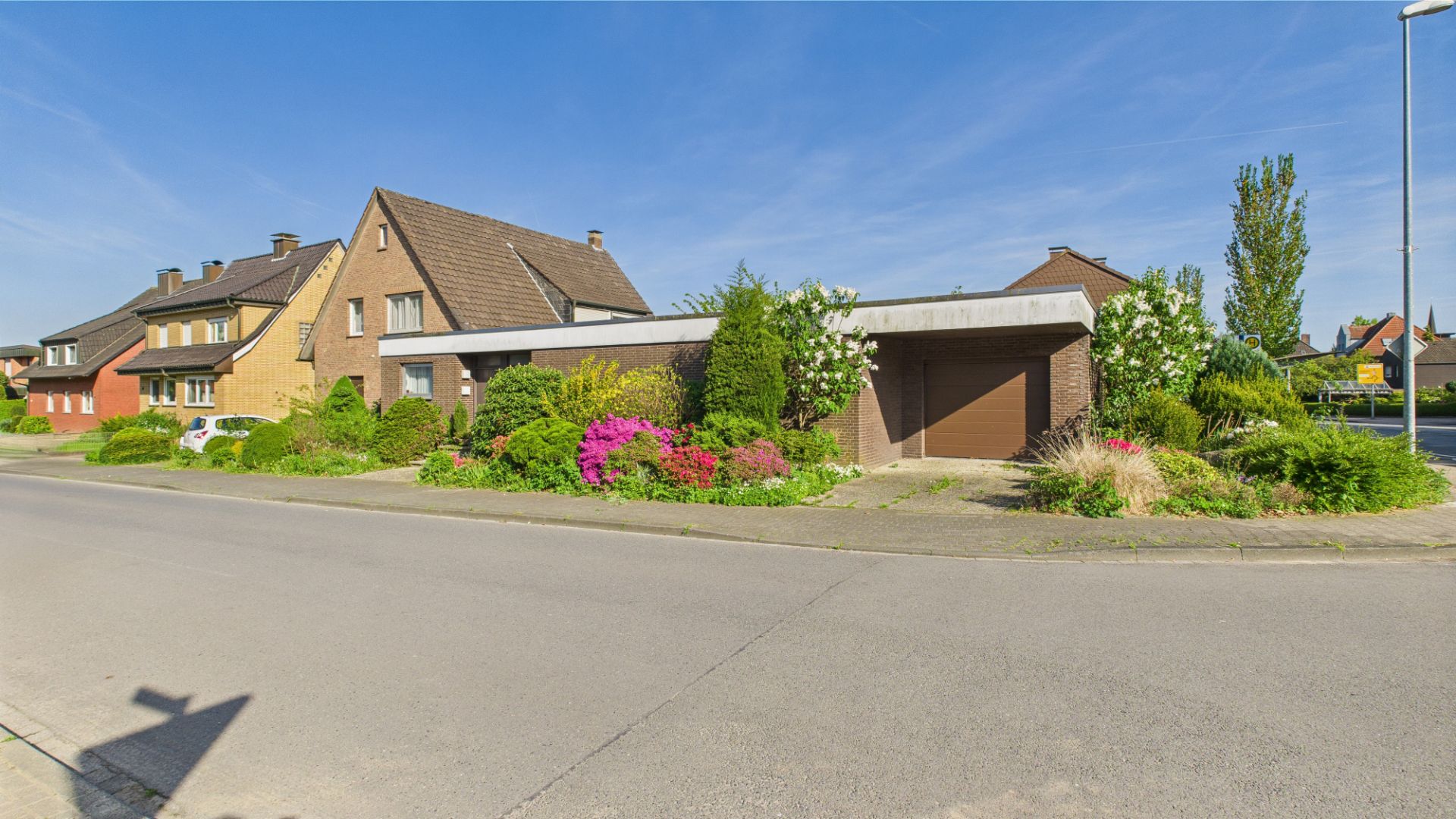 Wohnhaus mit Garage und gepflegtem Vorgarten, Blumen und Sträuchern an einer ruhigen Straße.