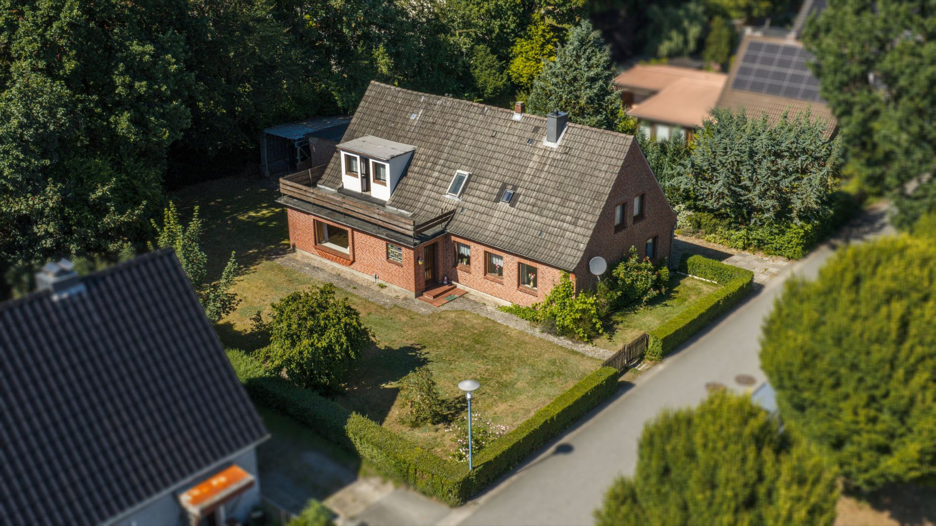 Backsteinhaus mit Garten, Hecke und Bäumen, aus der Vogelperspektive fotografiert.