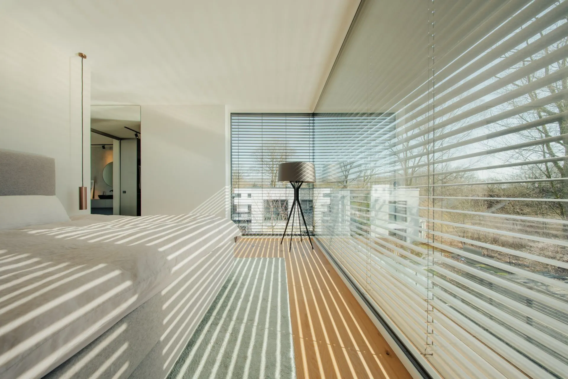 Modernes Schlafzimmer mit großem Fenster, Jalousien, Teppich und Stehlampe.