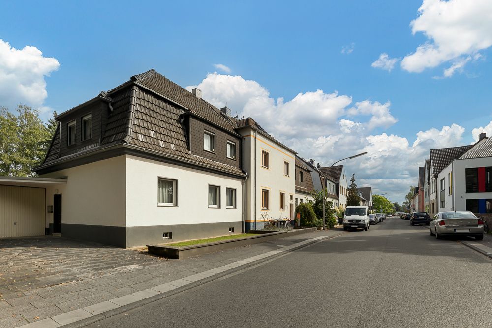 Wohnhäuser an einer ruhigen, sauberen Straße mit parkenden Autos und einigen Bäumen.