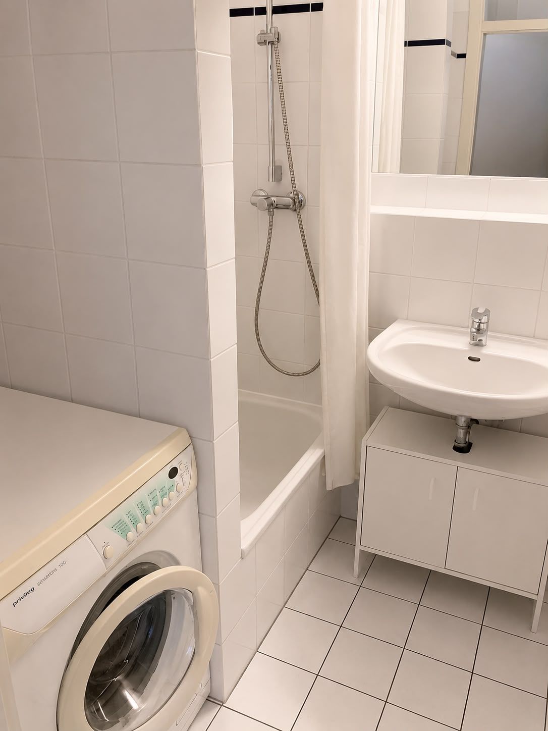 Badezimmer mit Waschmaschine, Badewanne mit Duschvorhang und Waschbecken mit Spiegel.