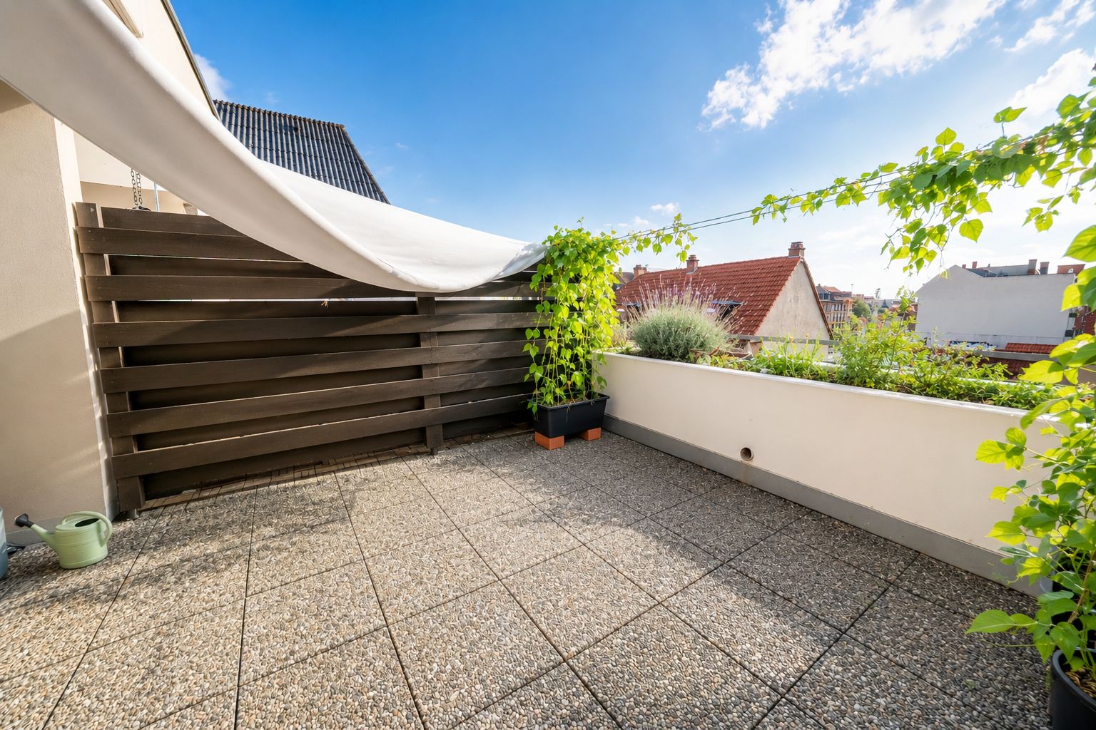 Sonnige Terrasse mit Fliesenboden, Holzsichtschutz und einigen Pflanzen in Töpfen.