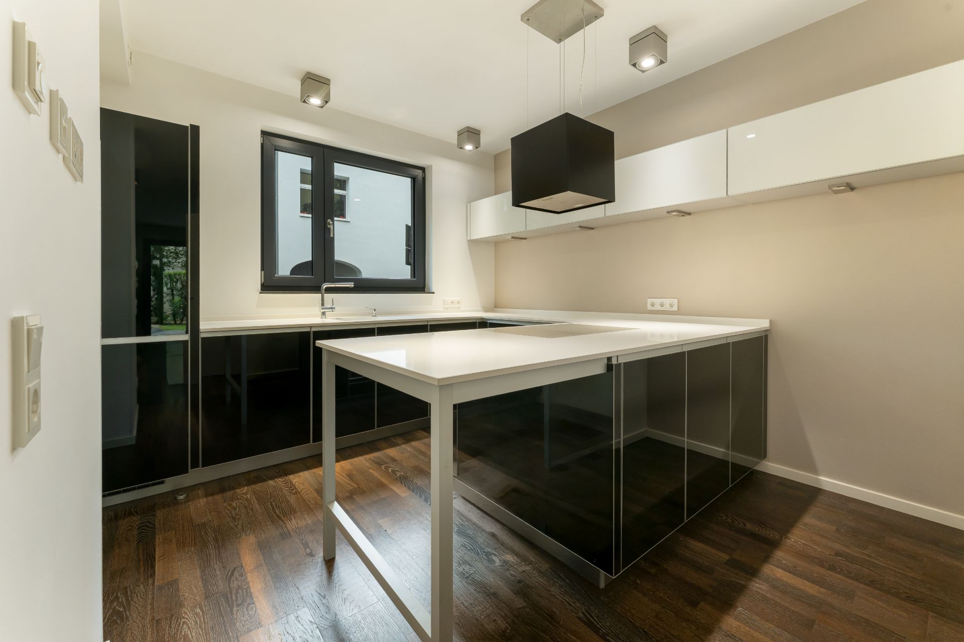 Moderne Küche mit dunklem Boden, weißen Arbeitsflächen und großen Fenstern.