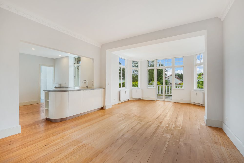 Helles Wohnzimmer mit Holzfußboden, offener Küche und großen Fenstern mit Blick nach draußen.