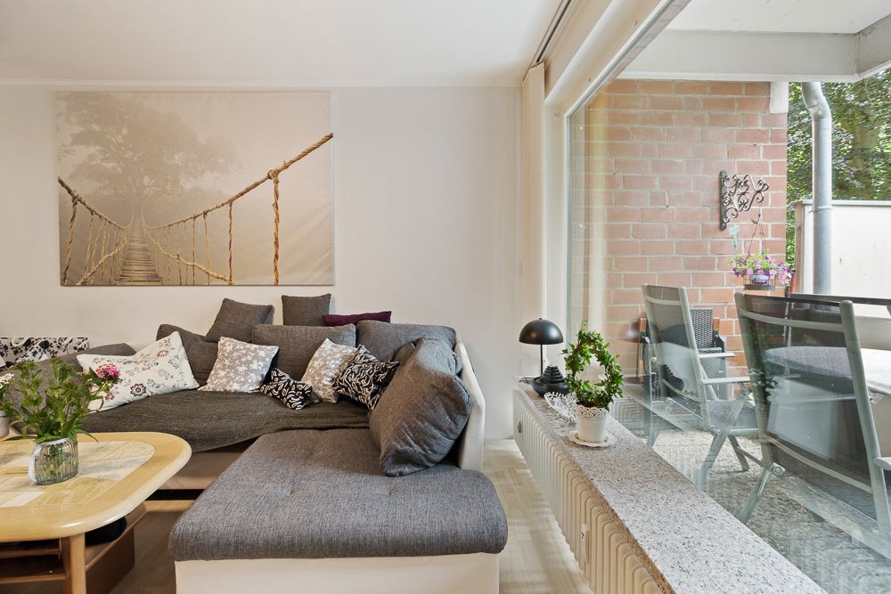 Wohnzimmer mit grauem Sofa, Couchtisch, großem Fenster und Blick auf Terrasse mit Tisch und Stühlen.